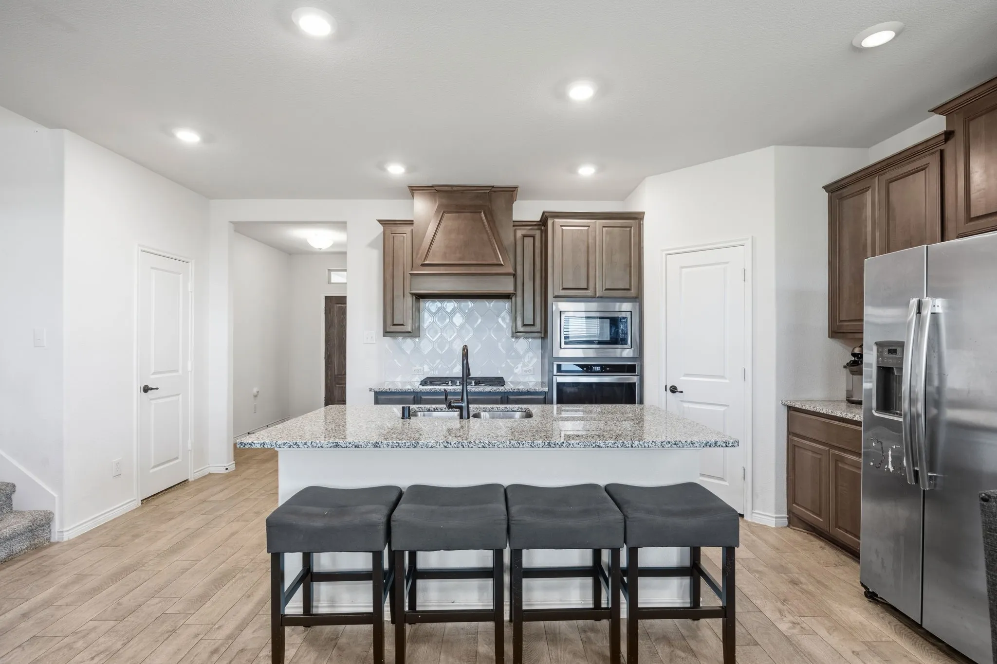 Kitchen featuring a large island with a granite countertop, wood-finish tile flooring, recessed lighting, built-in stainless steel appliances, and wood cabinetry