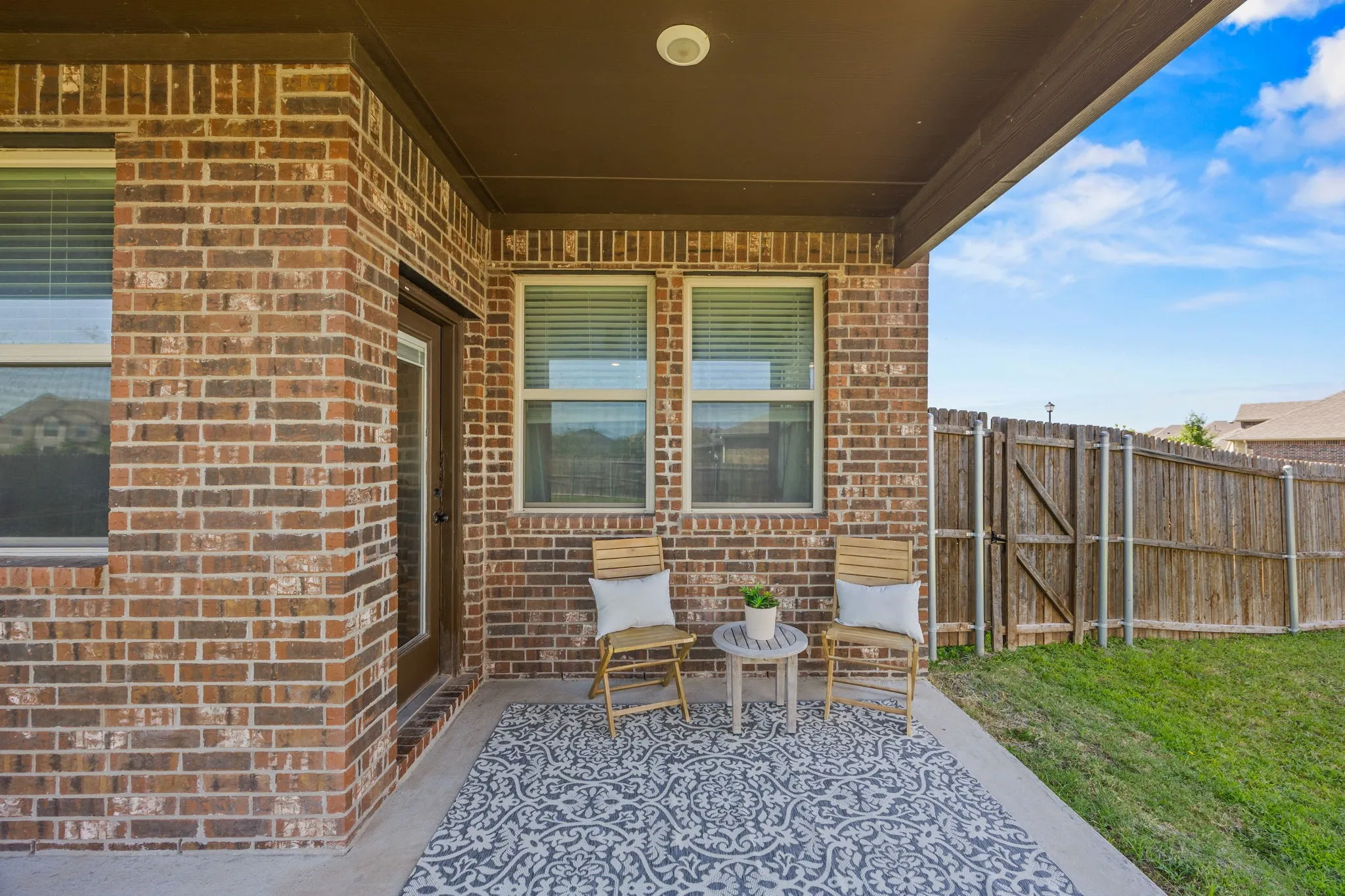 Covered patio area featuring brick exterior, concrete slab, and a wood privacy fence