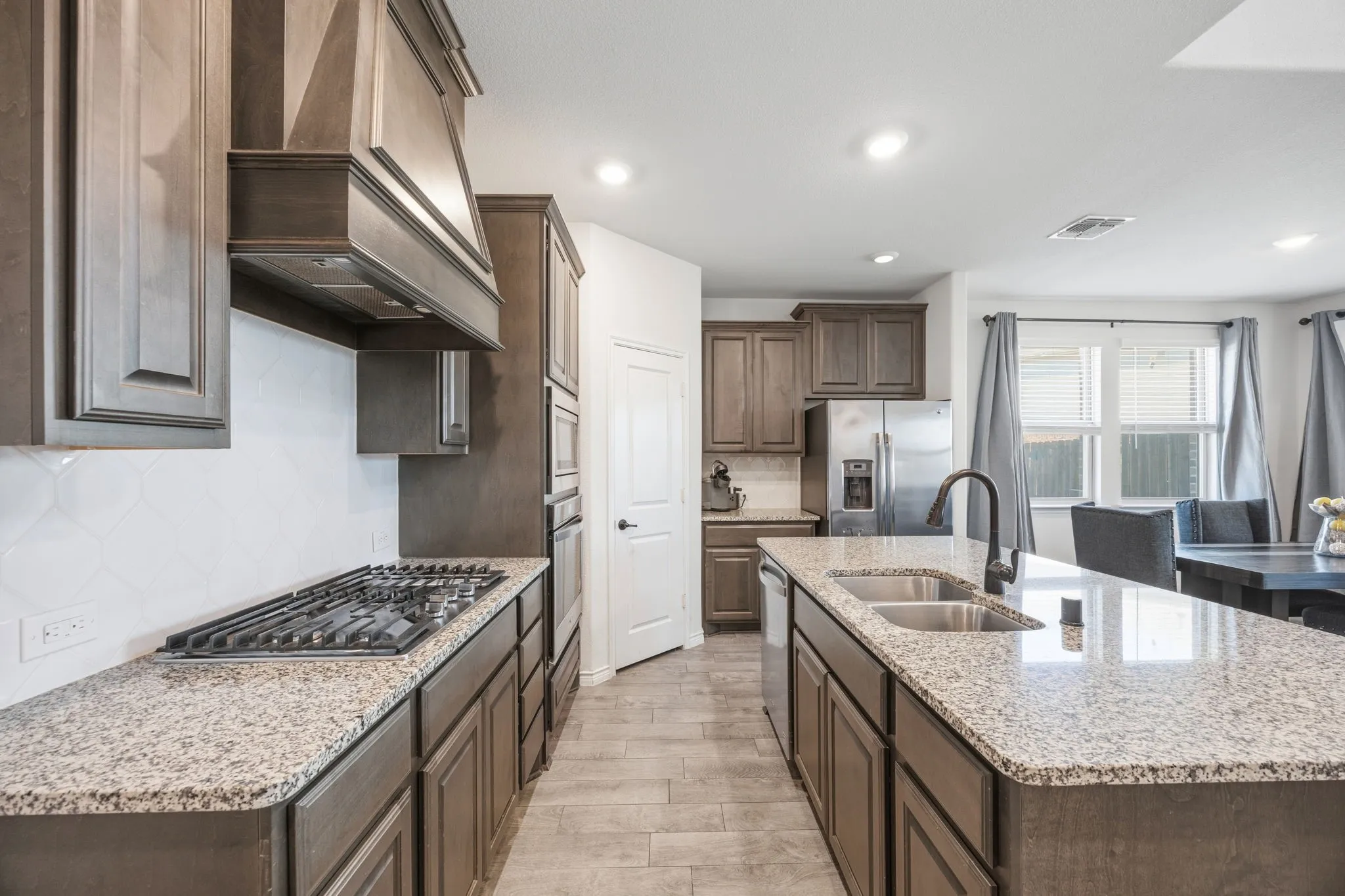 Kitchen featuring granite countertops, dark wood-finish cabinetry, stainless steel appliances, a gas cooktop, and a double basin sink