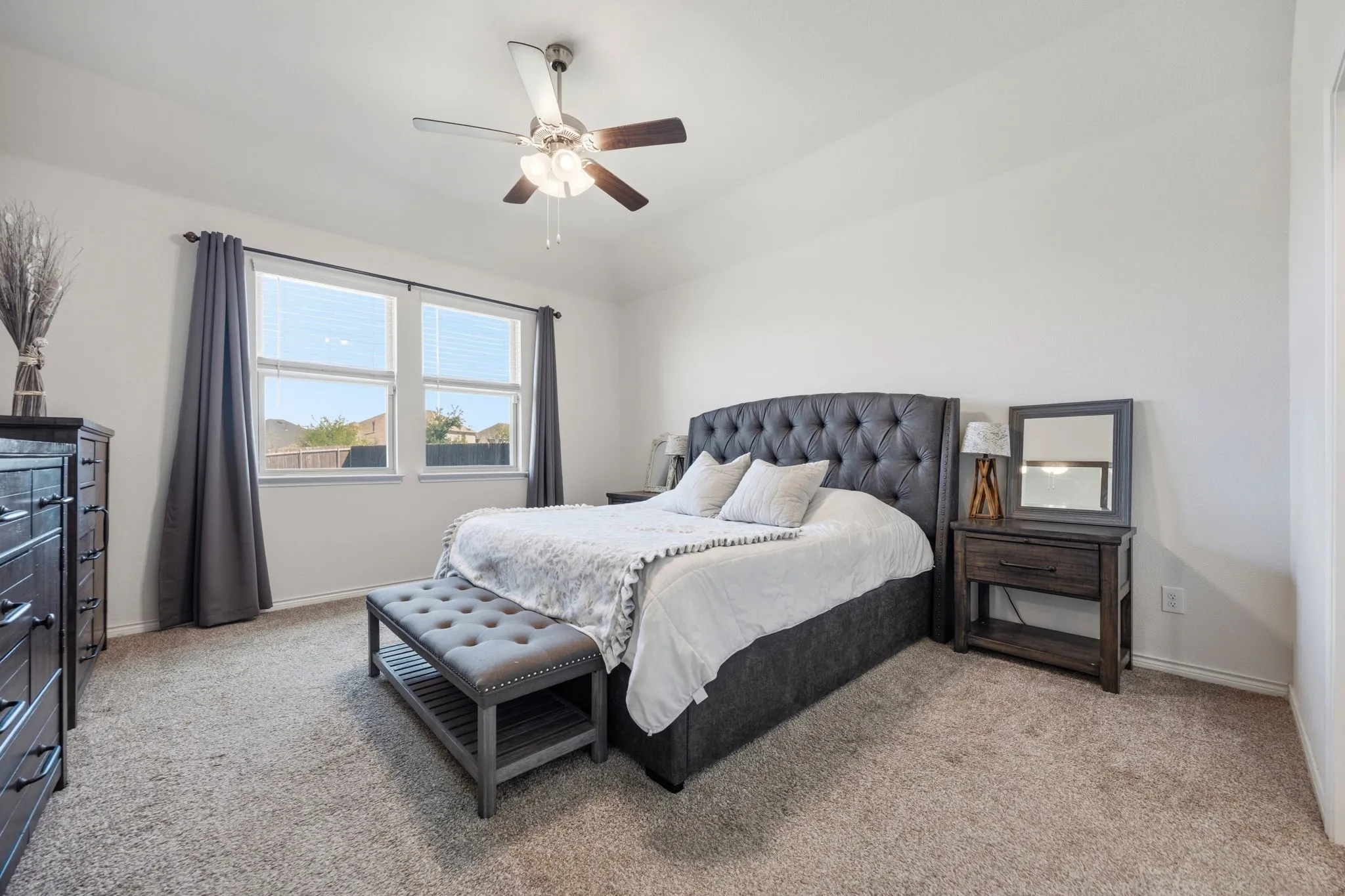 Large primary bedroom featuring a ceiling fan with light fixture, two windows with blinds, and white painted walls