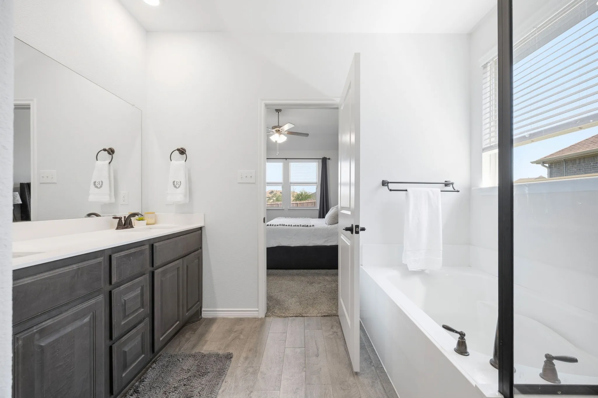 Primary bathroom featuring a rectangular soaking tub, dual vanity with dark wood-finish cabinetry, light-toned countertop, and wood-finish flooring