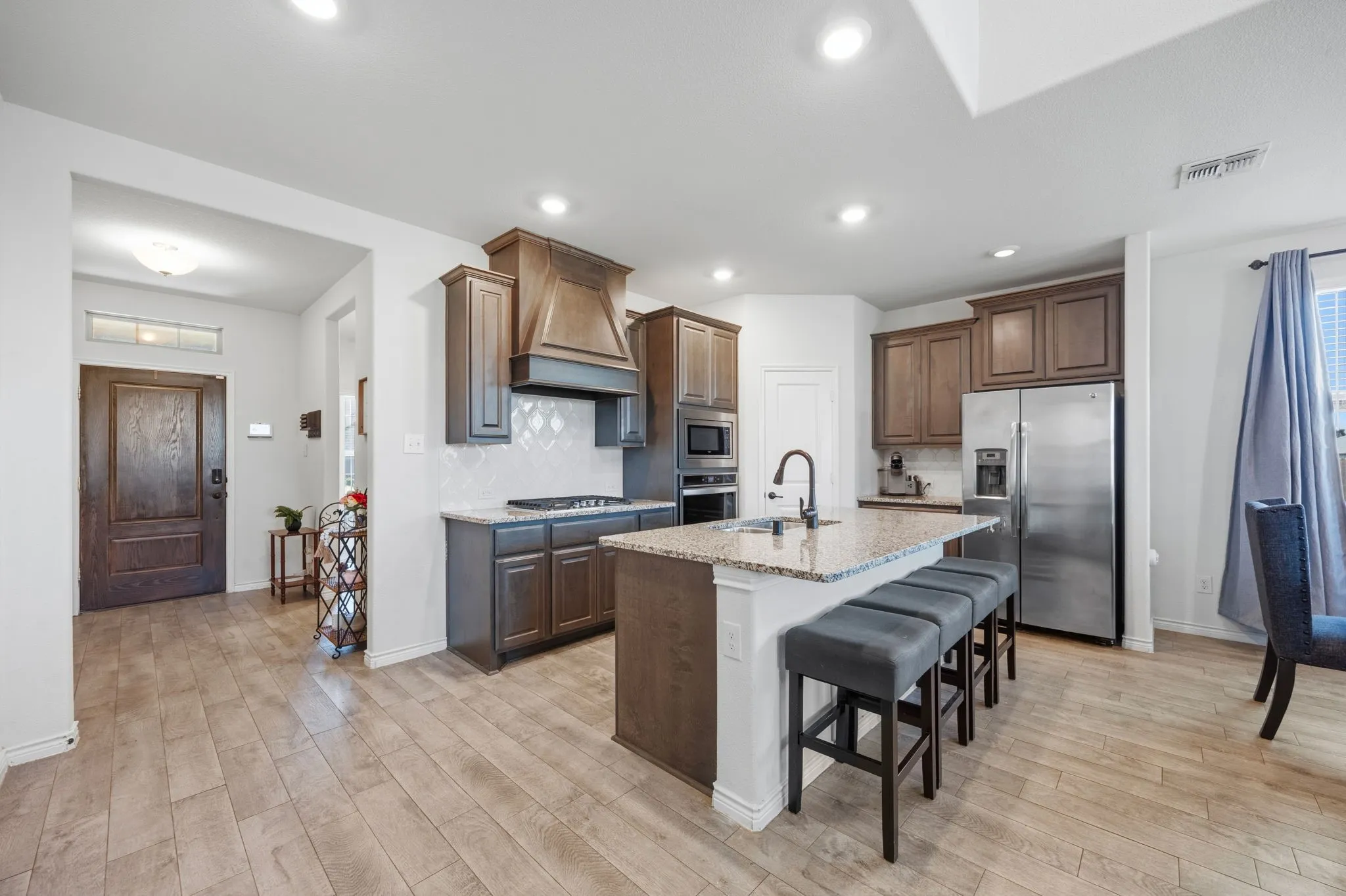 Contemporary kitchen featuring dark wood cabinetry, stainless steel appliances, granite countertops, and a center island with bar seating