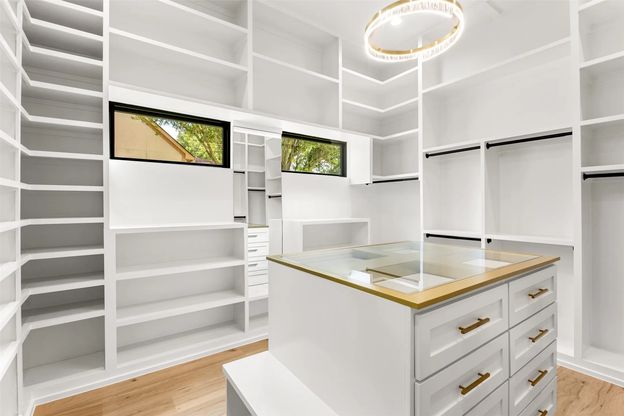 Spacious walk-in closet featuring extensive built-in shelving, hanging rods, and a central island with drawers and a glass top