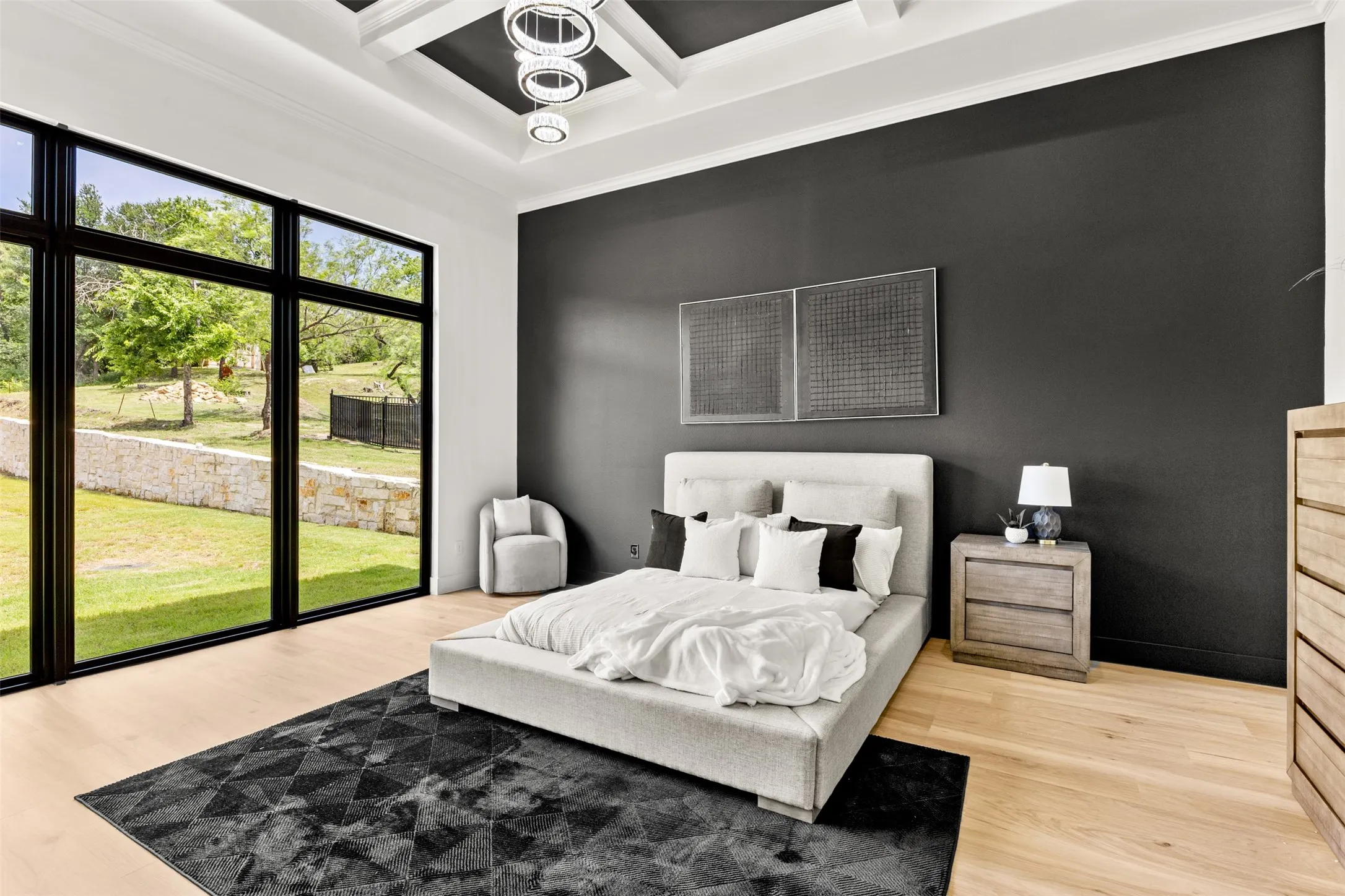 Expansive floor-to-ceiling windows with black frames, wood-finish flooring, a coffered ceiling with a modern light fixture, a contrasting dark accent wall, and perimeter crown molding