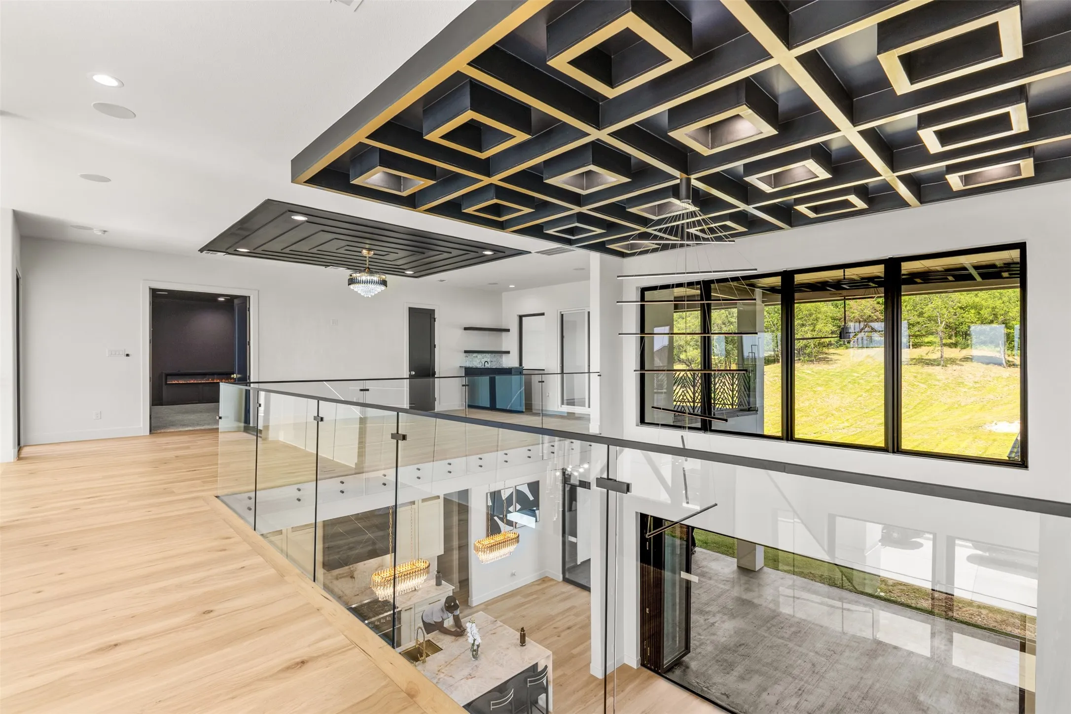 Hardwood flooring across an open-concept upper level, featuring glass railings and a coffered ceiling with integrated lighting
