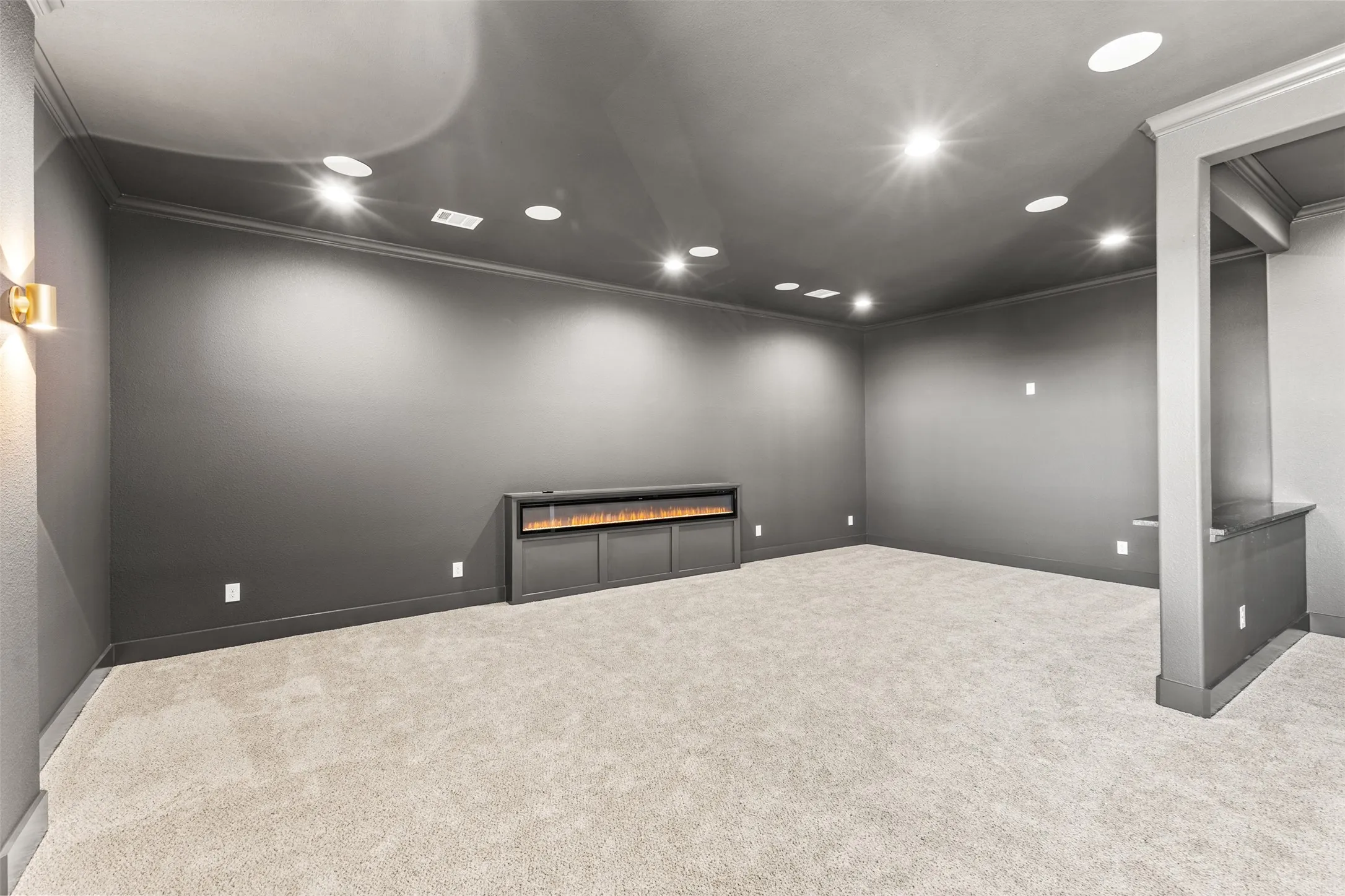 Spacious room featuring neutral carpeting, dark accent wall, recessed lighting, crown molding, and a built-in electric fireplace with cabinetry