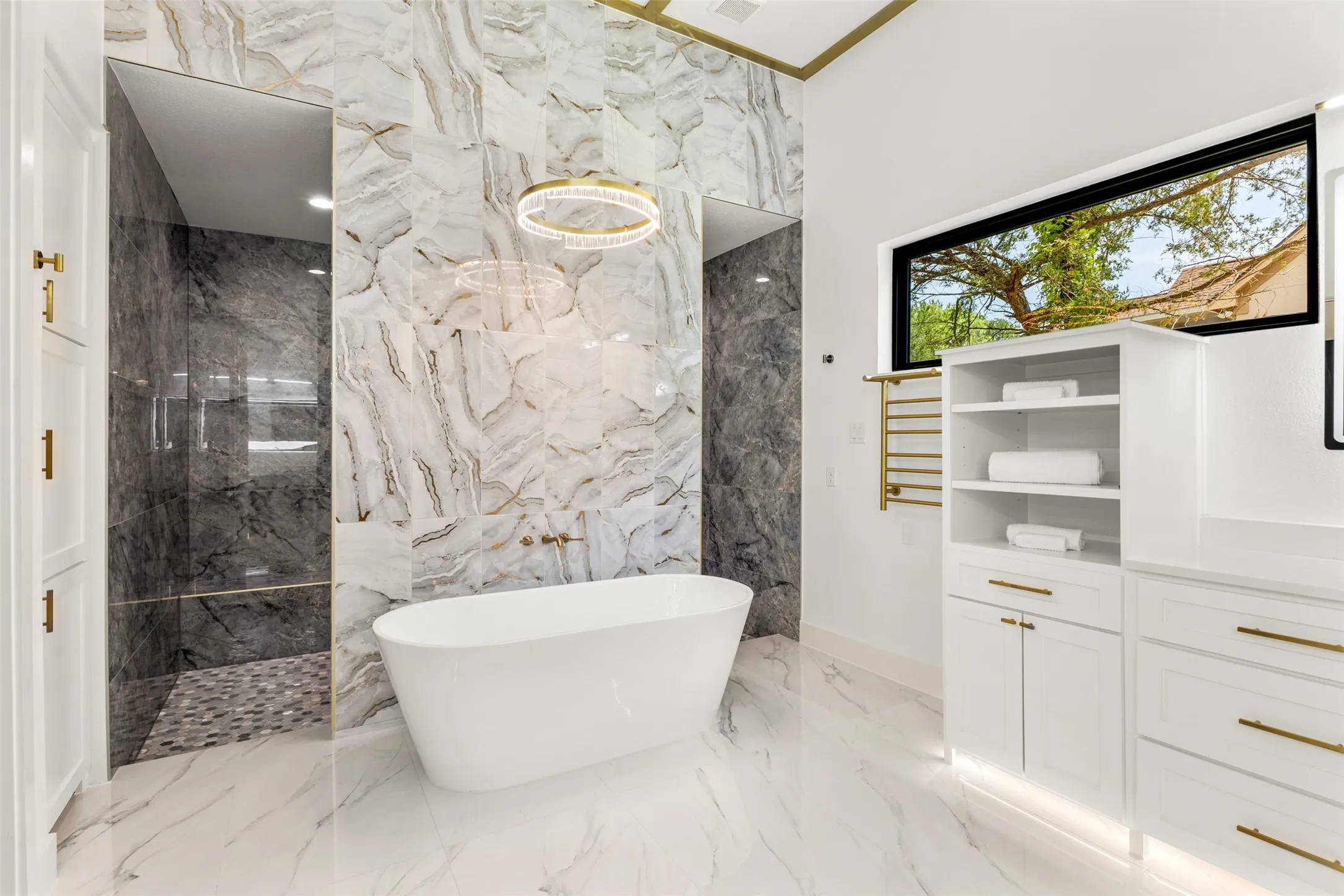 Freestanding soaking tub centered on a feature wall with full-height marble-look tile