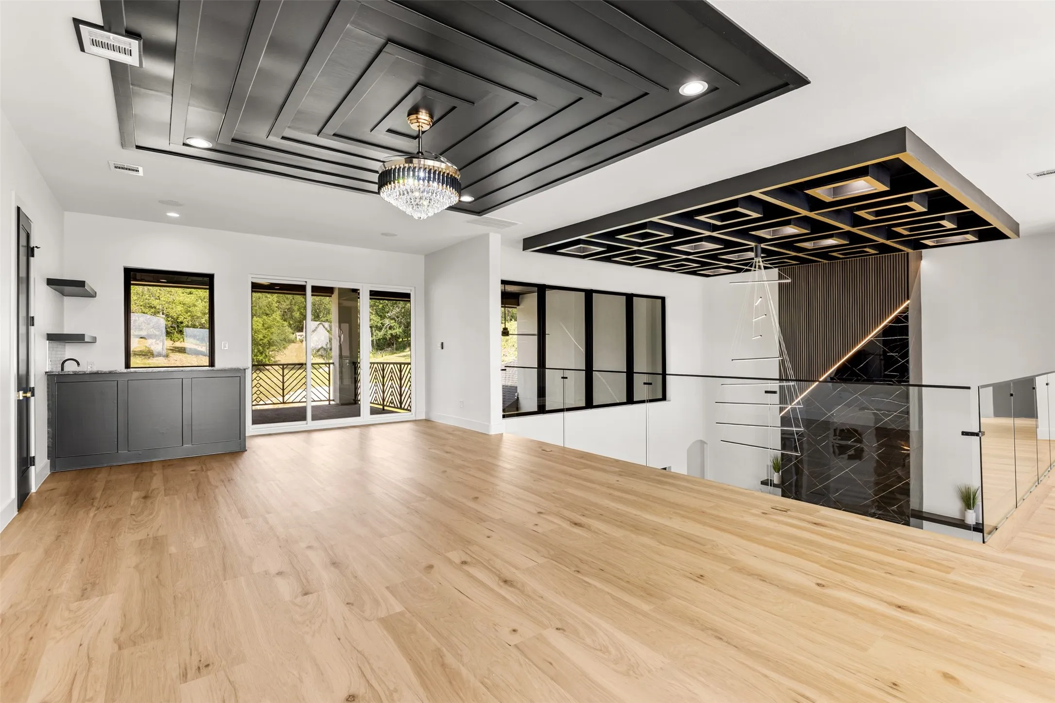 Spacious room featuring light wood-finish flooring, a coffered ceiling with a crystal chandelier, and a built-in wet bar with dark cabinetry