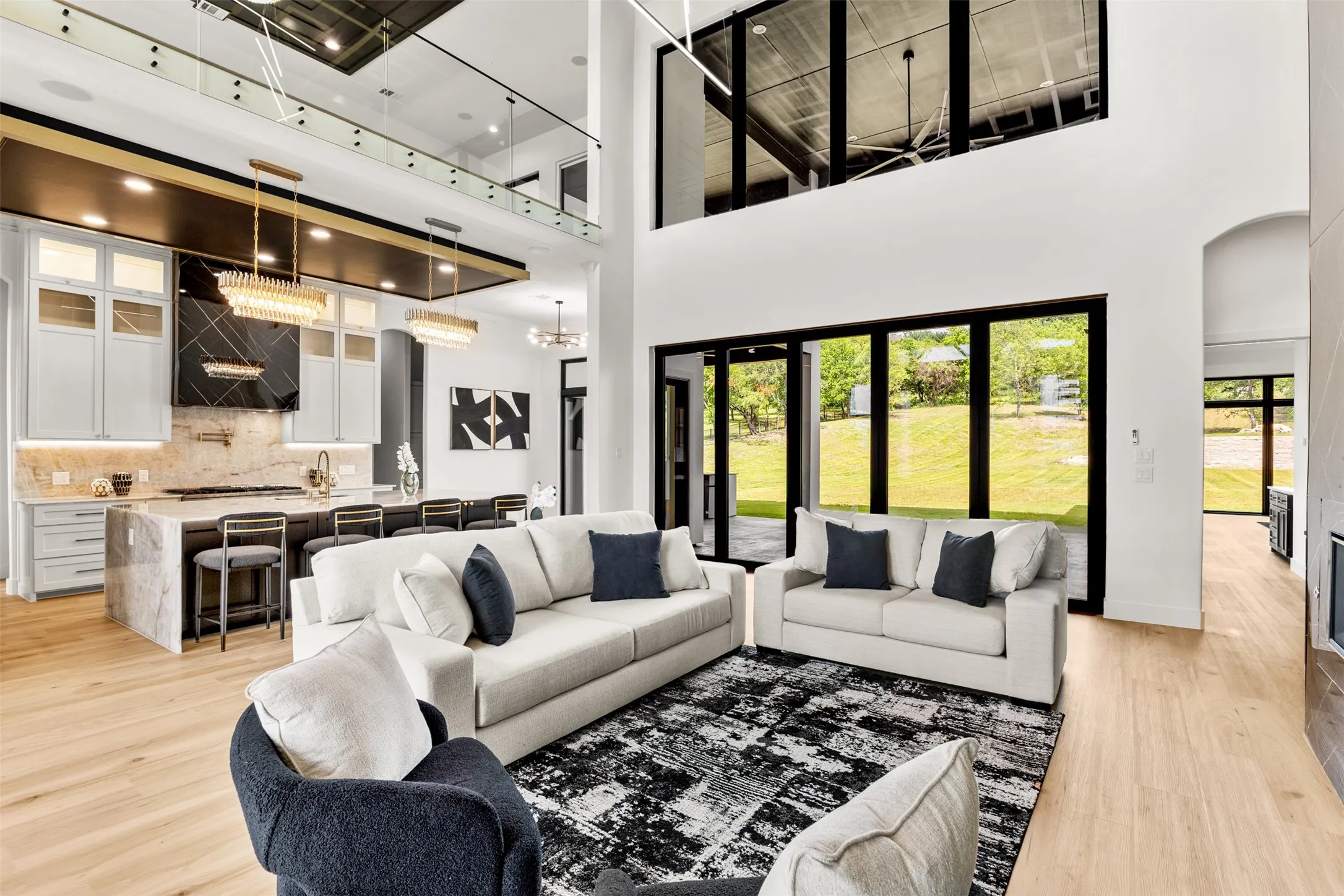 Vaulted living space with expansive floor-to-ceiling windows, light wood-finish flooring, and a contemporary kitchen featuring a large island with seating, pendant lighting, and a striking range hood