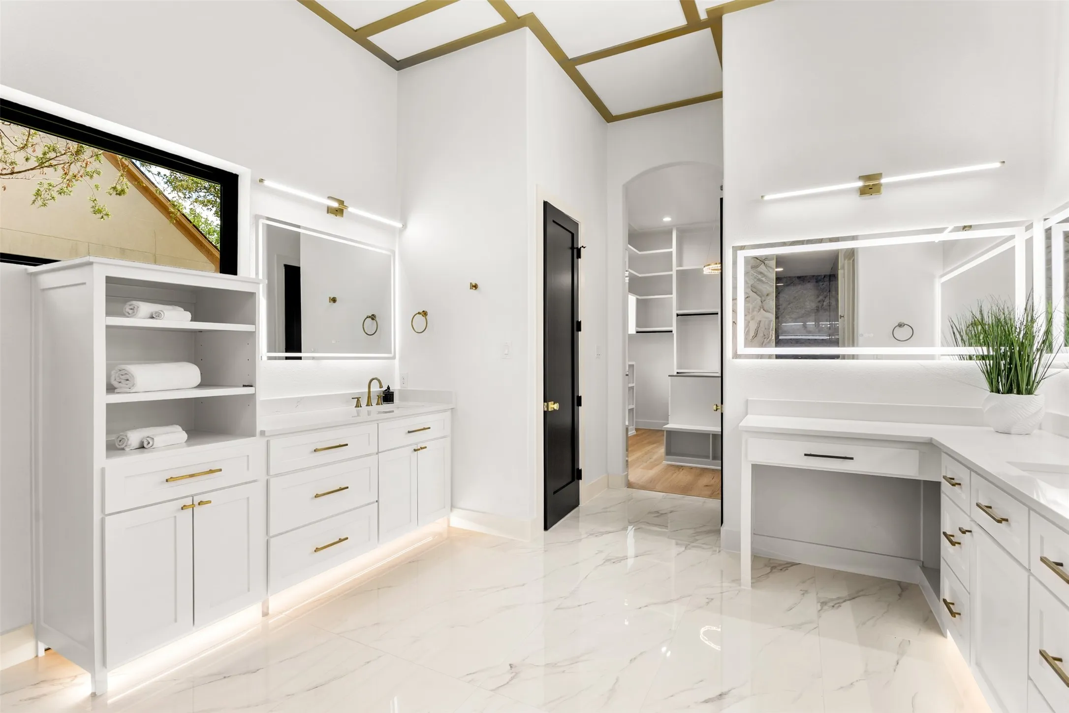 Spacious bathroom featuring white cabinetry with gold-toned hardware, under-cabinet lighting, and large format marble-look floor tiles