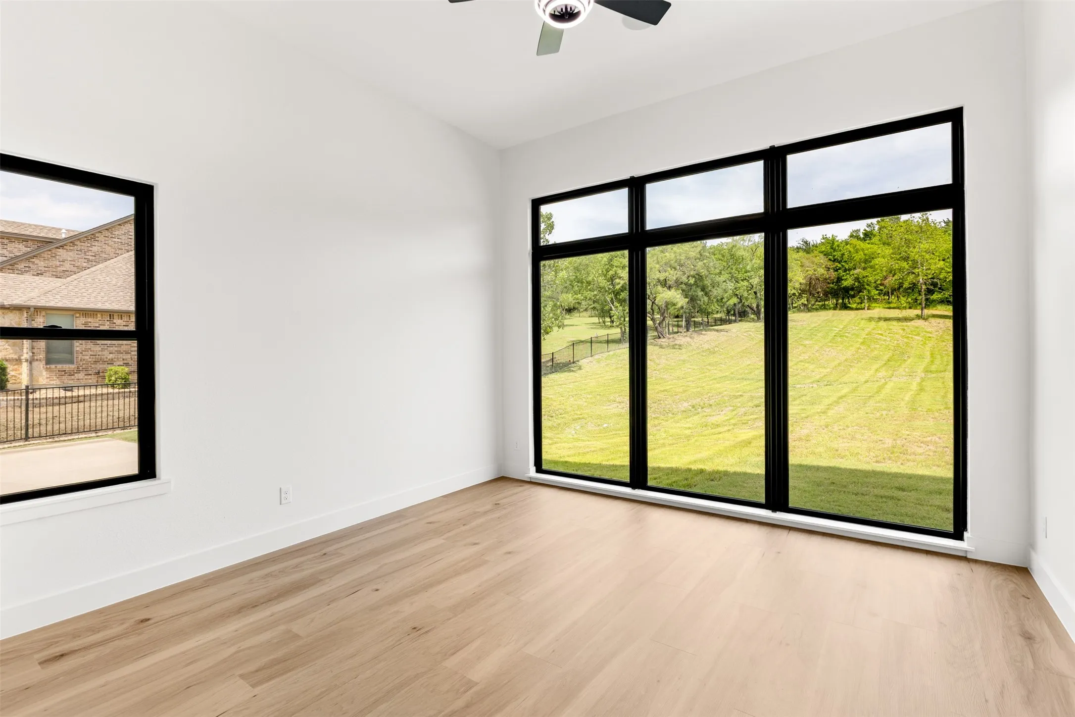 Expansive window wall with black framing, wood-finish flooring, crisp white walls, and a ceiling fan