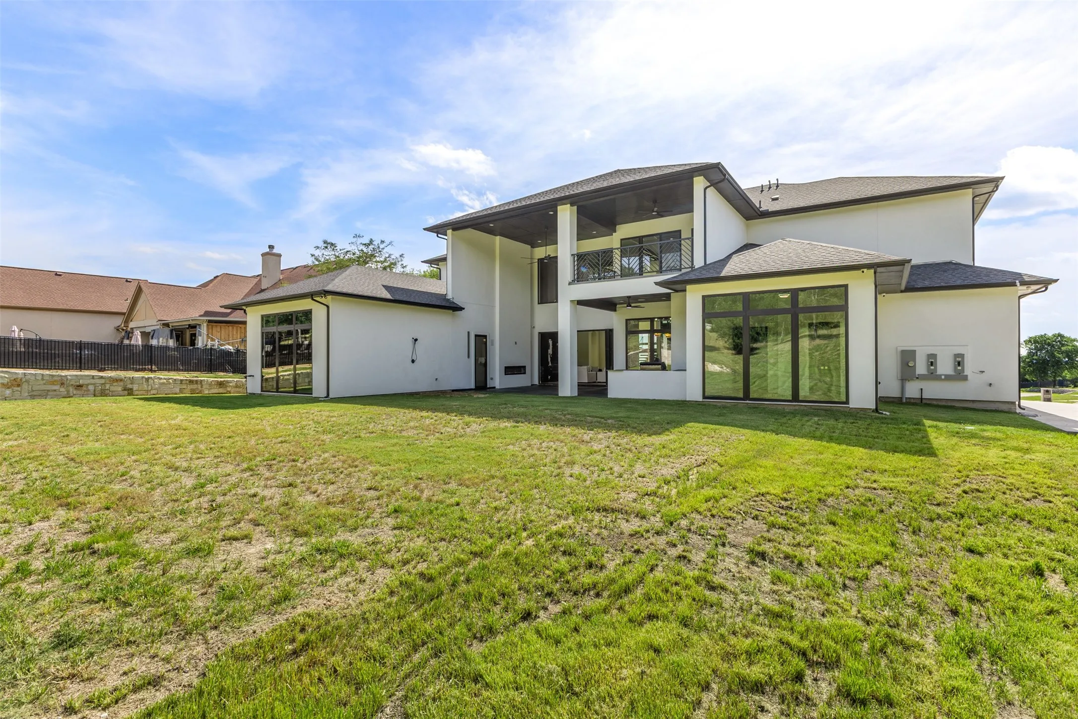 Rear exterior featuring a covered patio, upper-level balcony, and expansive glass panels