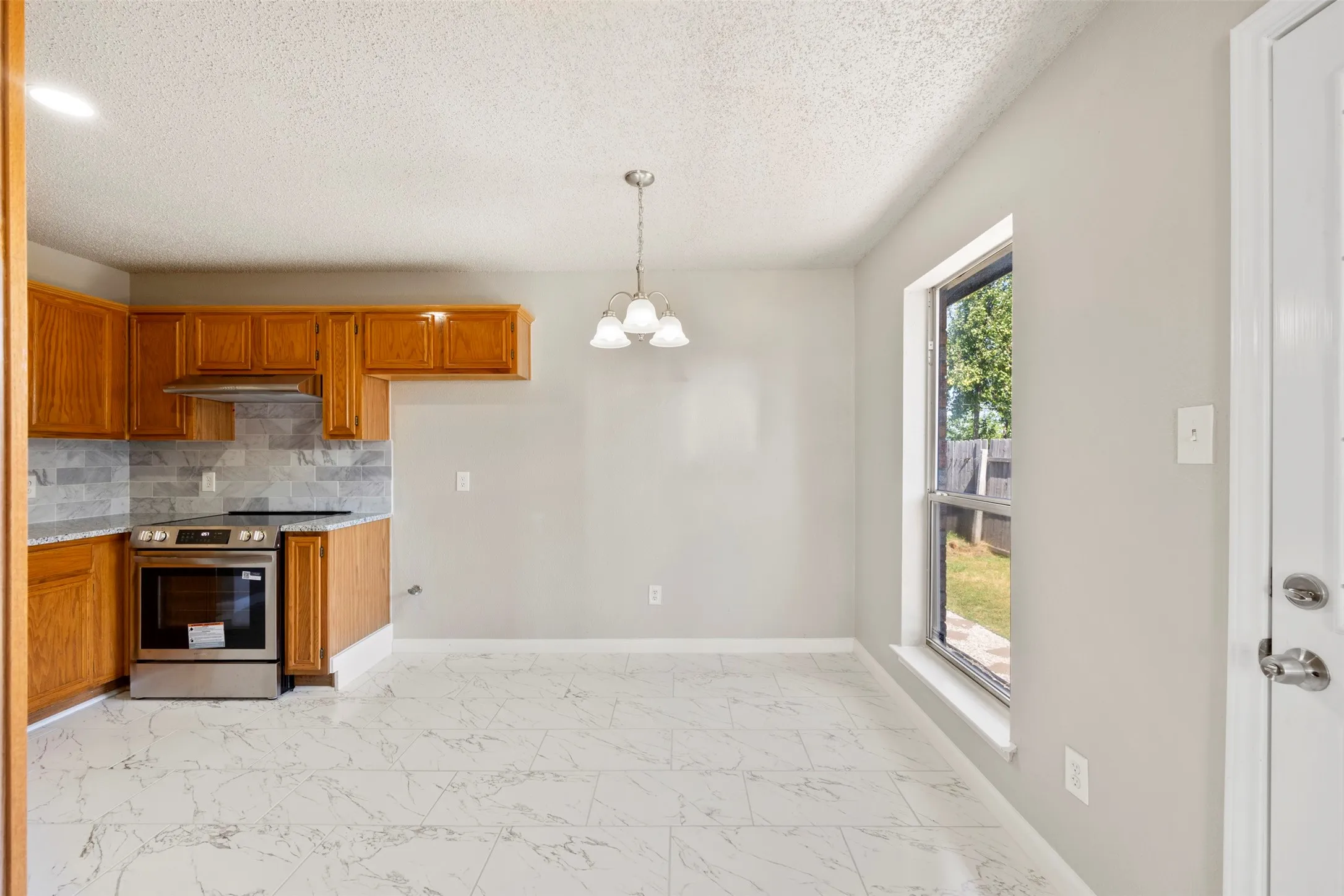 Kitchen and dining area featuring light wood cabinetry, stone-look backsplash, and stainless steel range