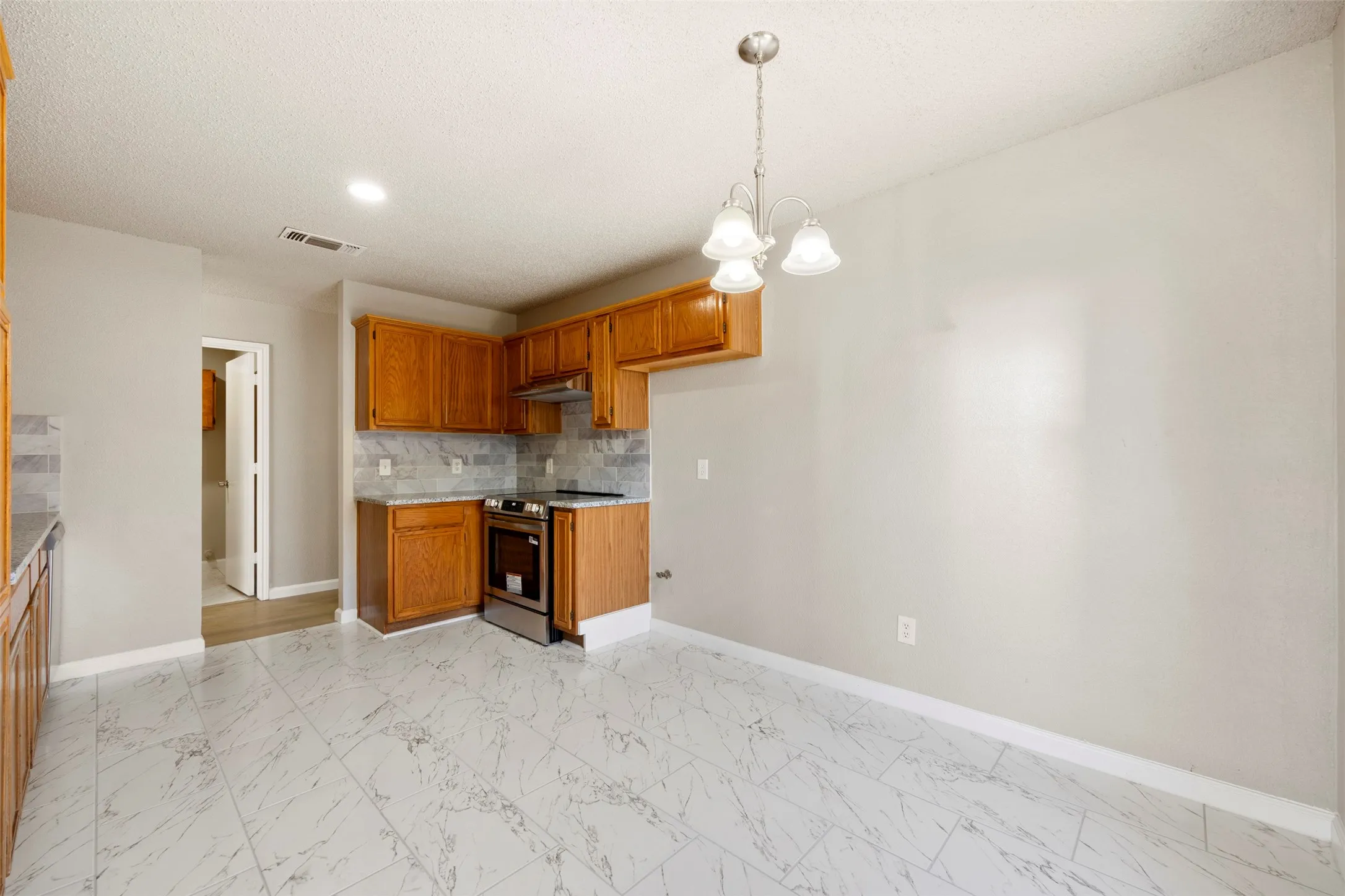 Kitchen and dining area featuring wood-finish cabinetry, stainless steel range, gray subway tile backsplash, and marble-look floor tiles