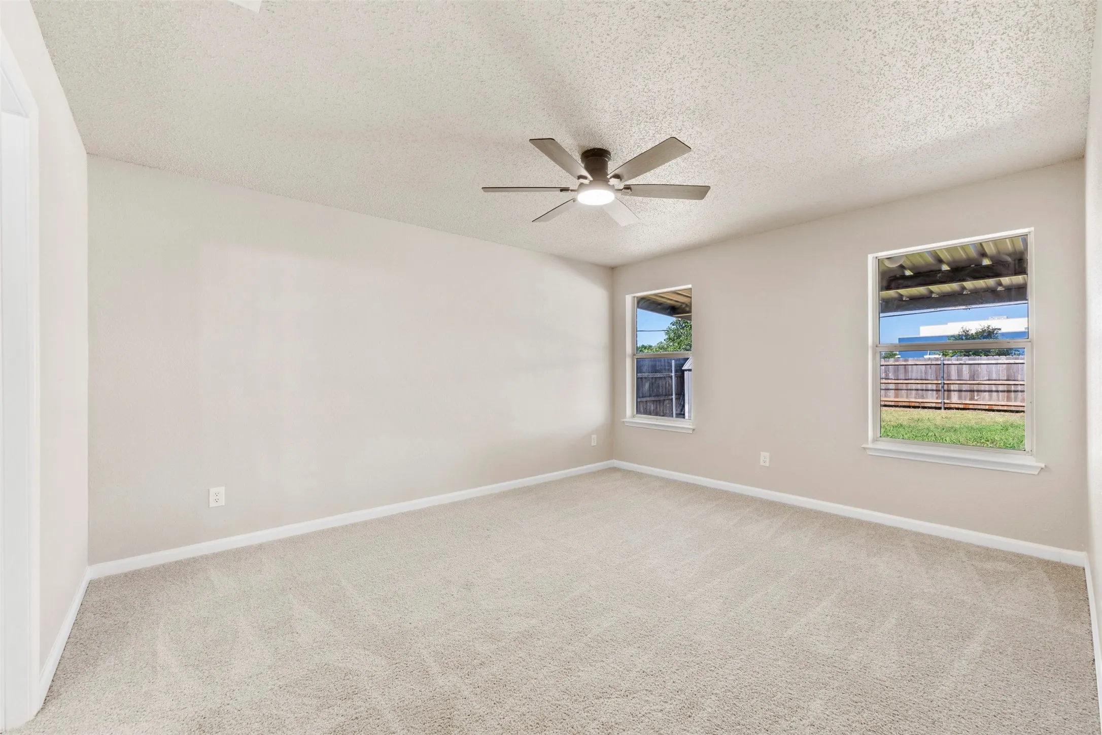 Spacious room featuring neutral paint, light-colored carpeting, two windows, and a ceiling fan with integrated lighting