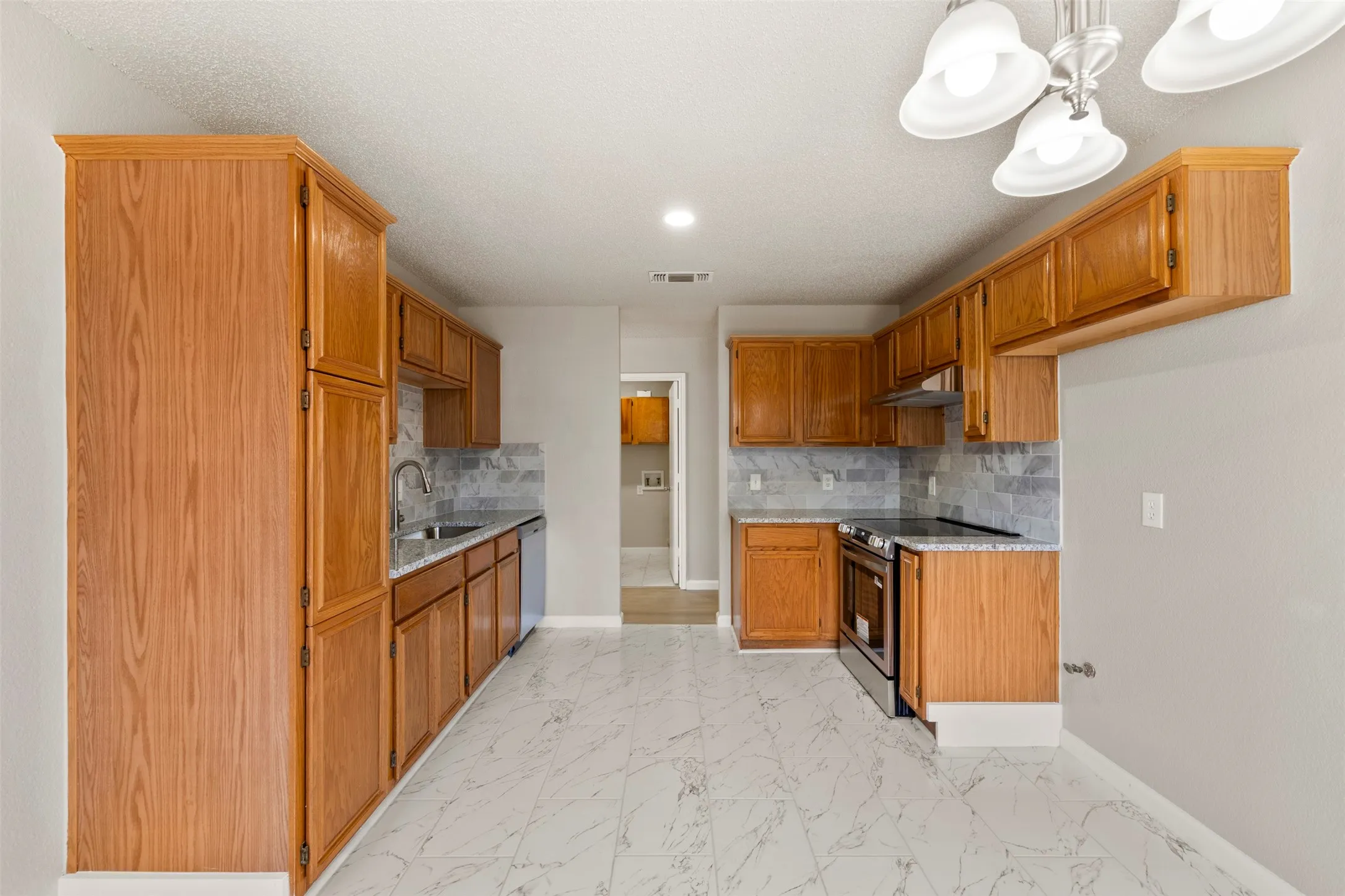 Spacious kitchen featuring extensive wood cabinetry, granite-style countertops, a stainless steel electric range, and a full tile backsplash