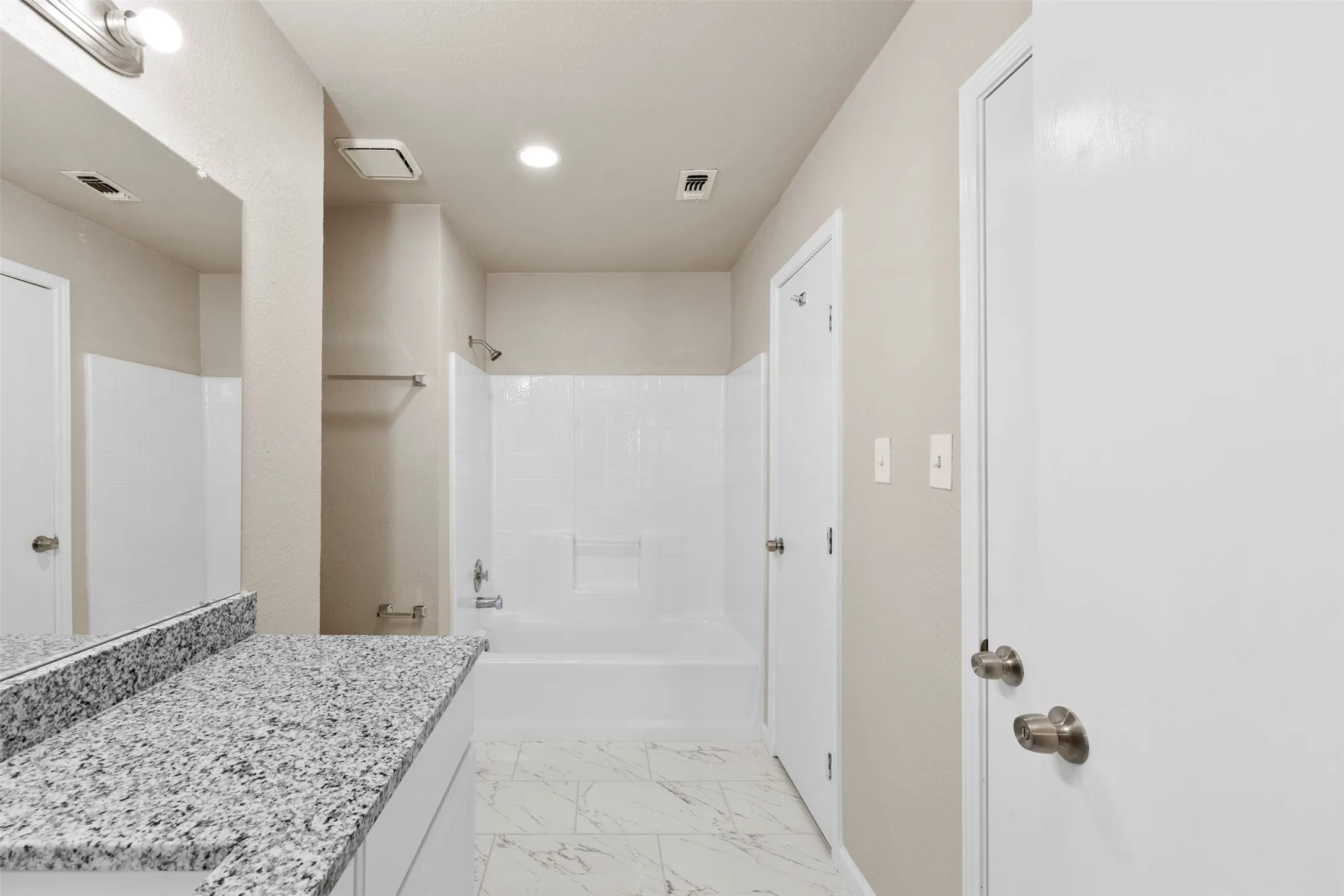 Bathroom featuring a granite-look countertop, white vanity, integrated bathtub with shower, white subway tile-patterned shower surround, and tile flooring