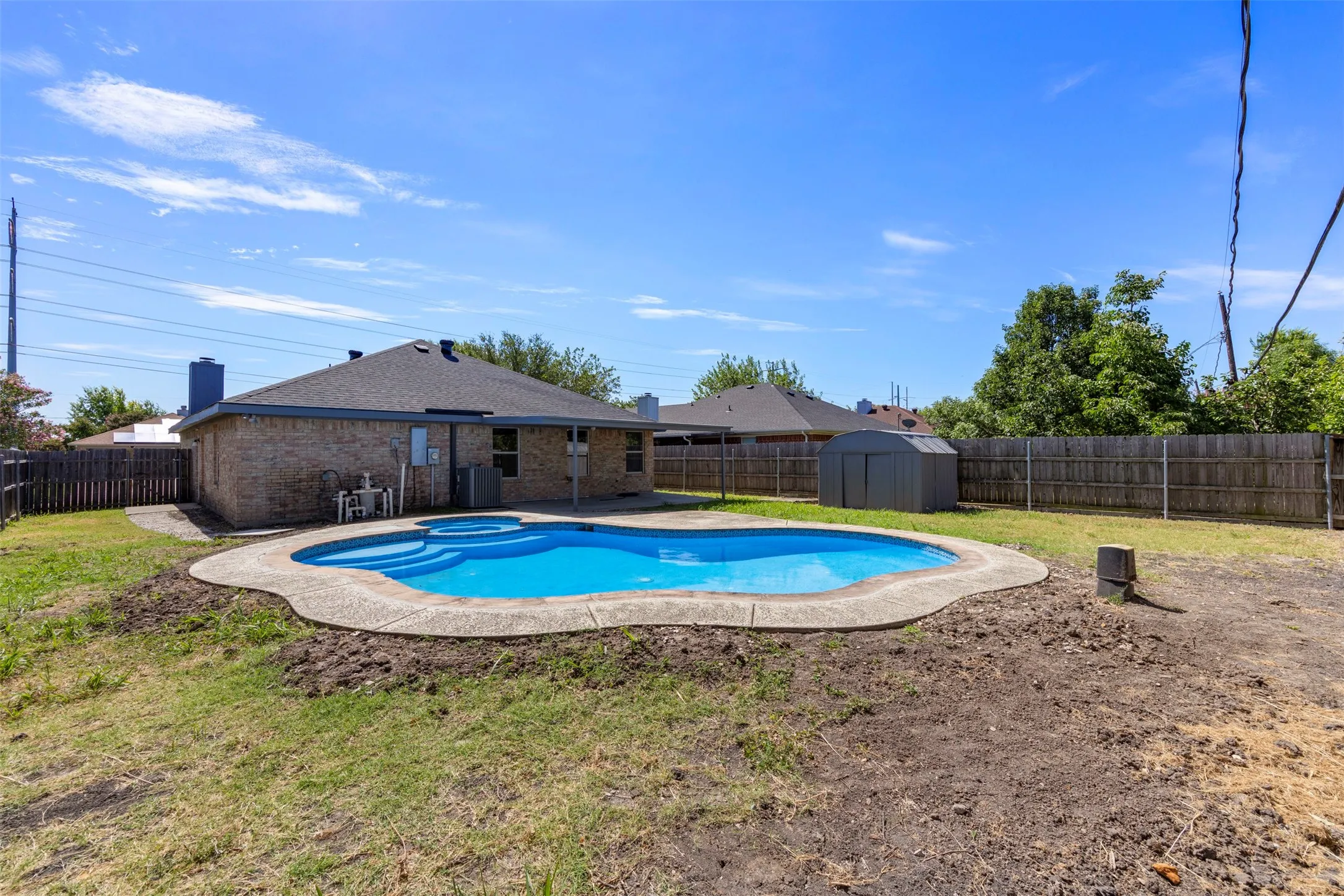 Expansive backyard featuring a built-in swimming pool with an integrated spa, concrete decking, and a brick-sided exterior