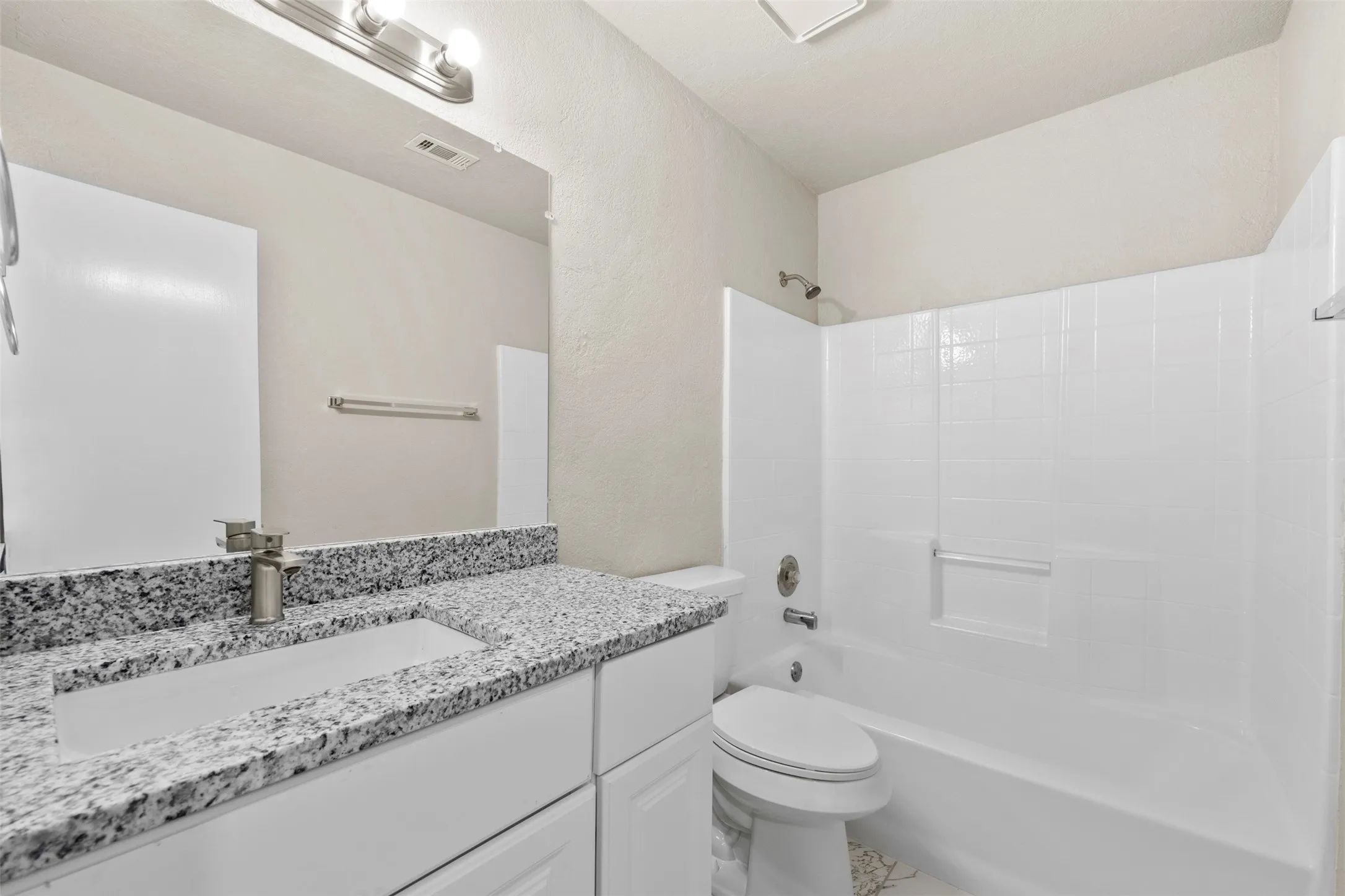 Bathroom featuring a white vanity with a speckled countertop, integrated rectangular sink, brushed nickel faucet, and a large wall-mounted mirror
