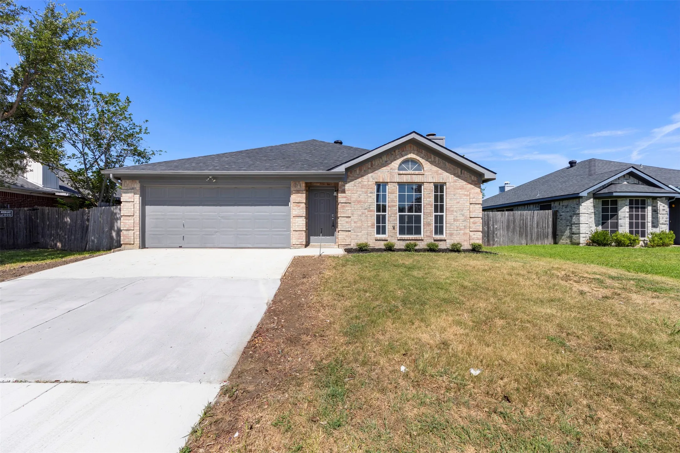 Brick facade home with an attached garage, featuring a concrete driveway, arched window details, and a shingled roof