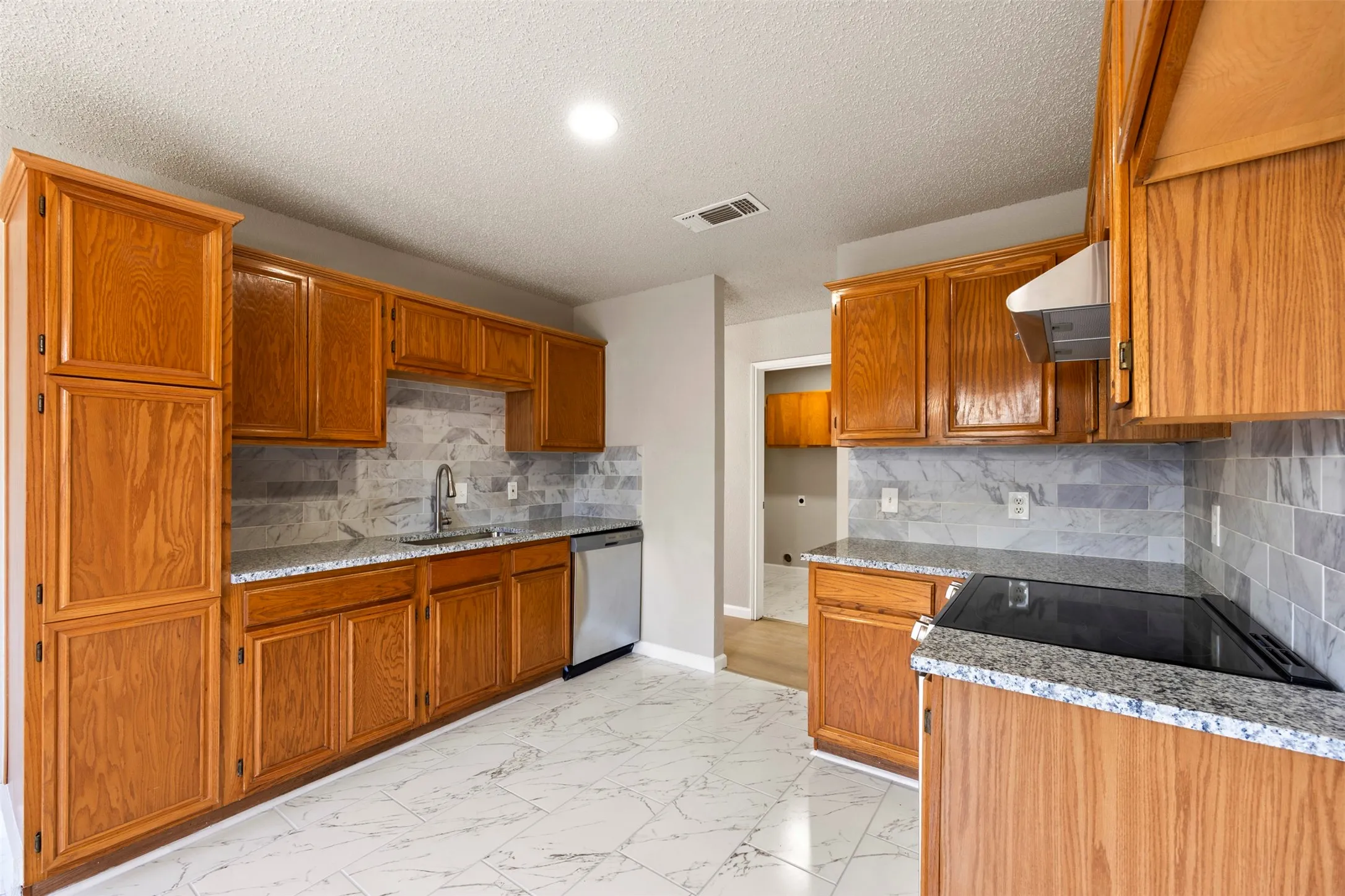 Kitchen featuring wood cabinetry, granite-finish countertops, subway tile backsplash, stainless steel sink, and stainless steel dishwasher