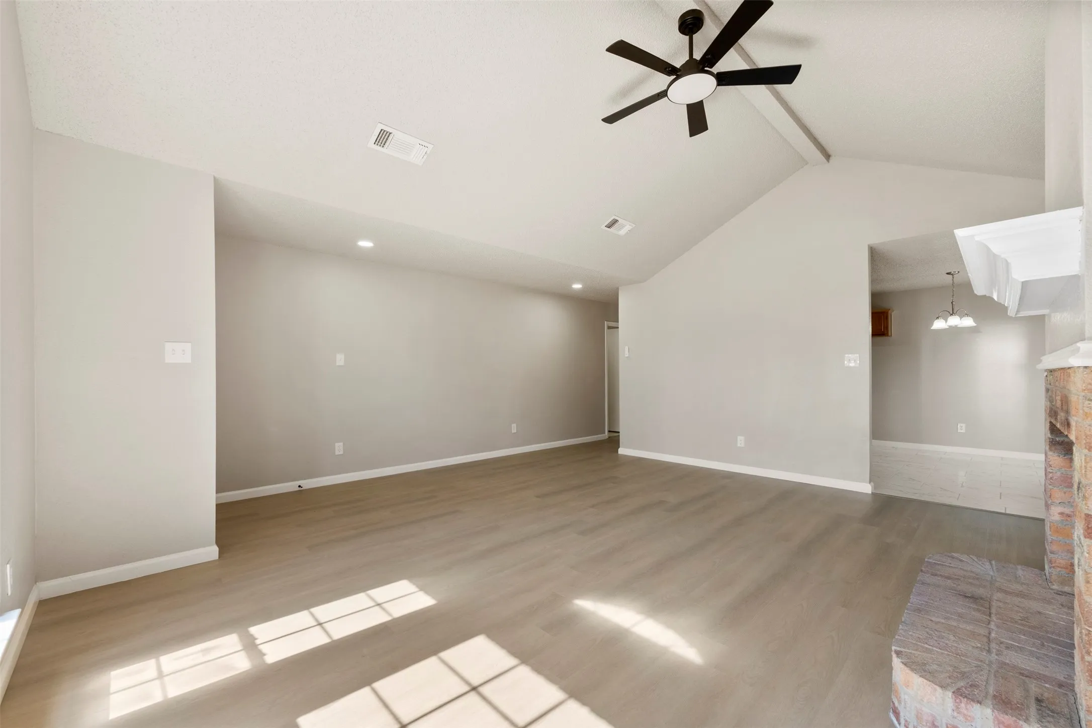 Spacious living area featuring vaulted ceilings, wood-finish flooring, recessed lighting, a ceiling fan, and a stone fireplace surround with a white mantle