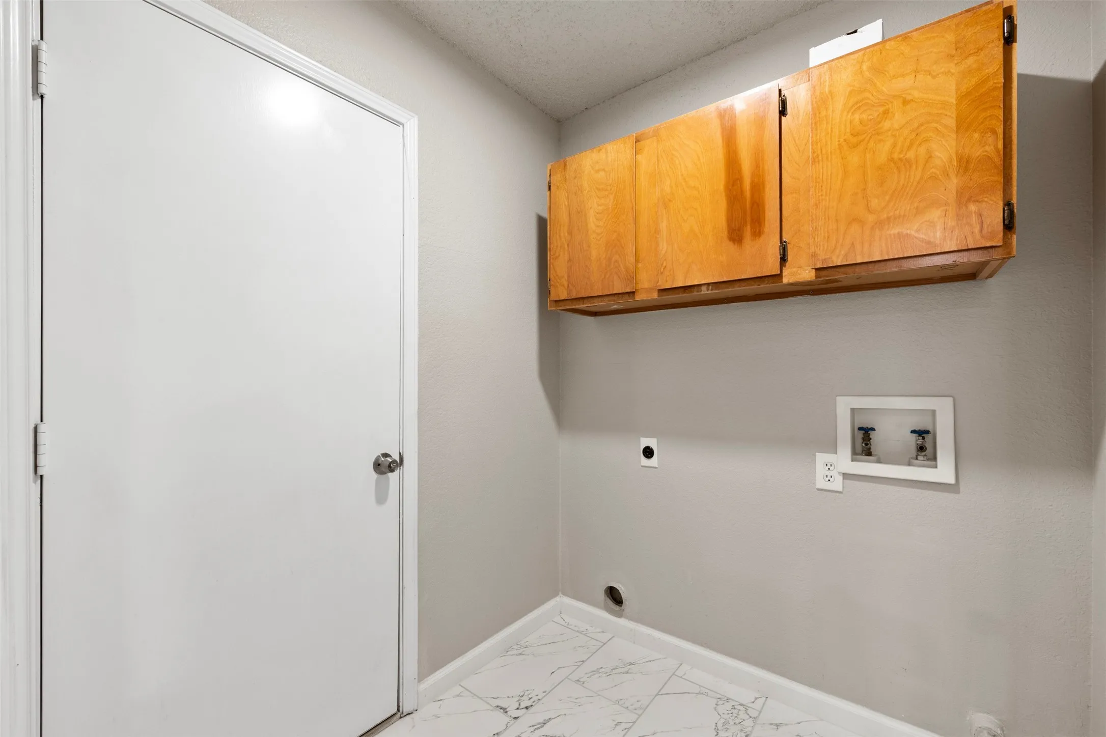Utility area featuring wood cabinetry, light grey wall paint, and white marble-look tile flooring
