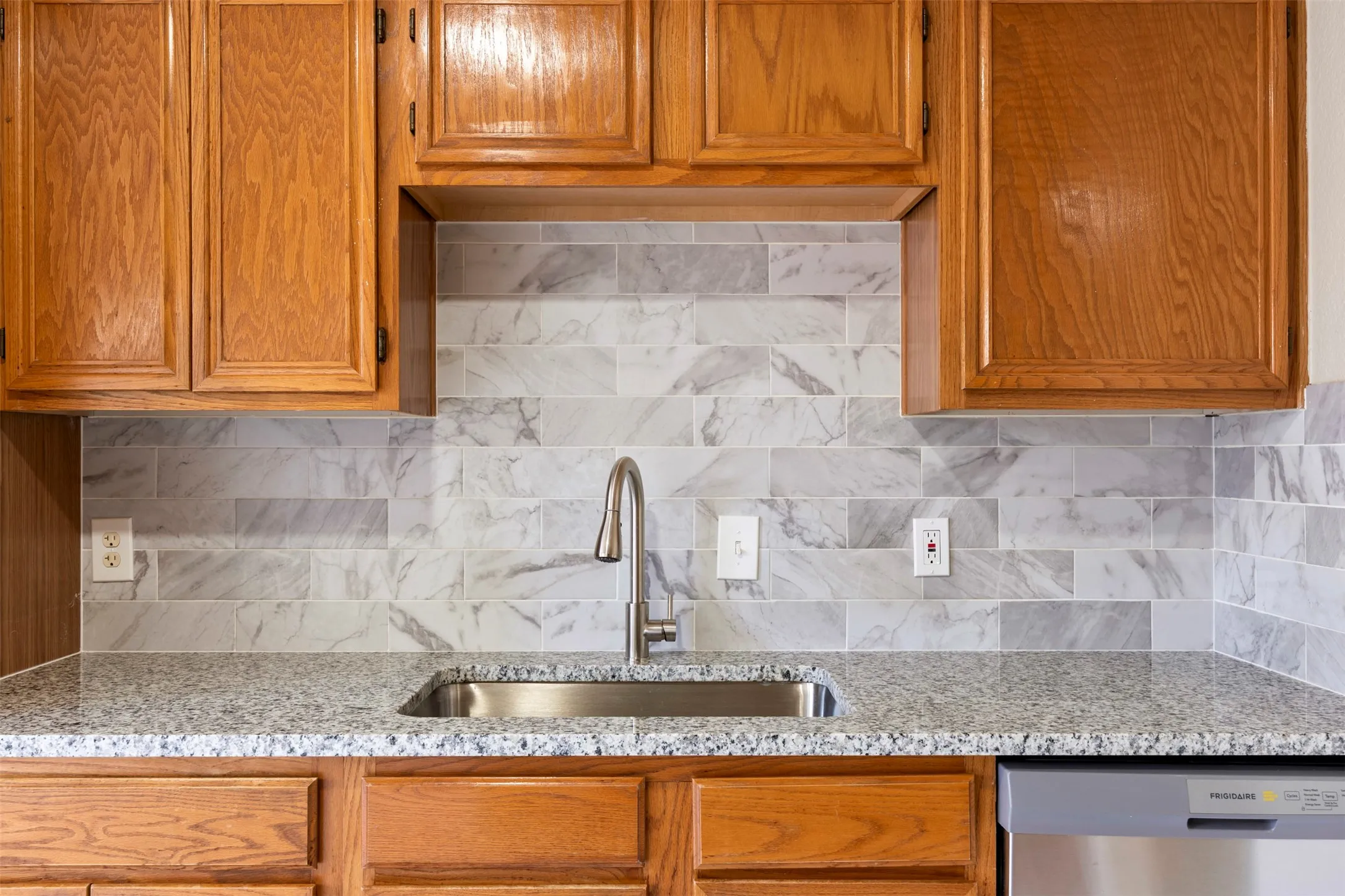 Kitchen featuring granite countertops, a stainless steel sink with a gooseneck faucet, a subway tile backsplash, and wood cabinetry