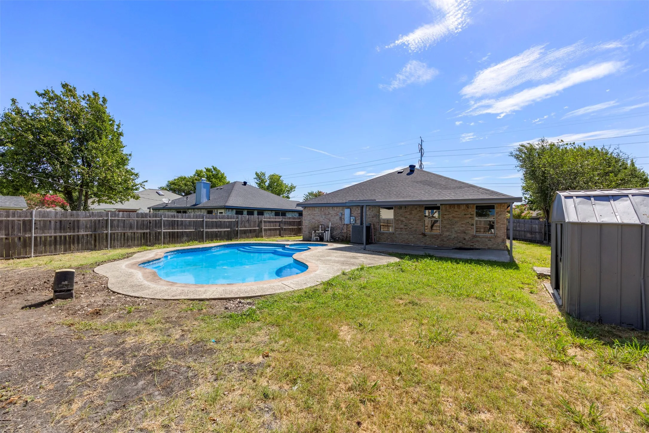 Rear exterior featuring a swimming pool with concrete surround, a brick facade, a covered patio, a privacy fence, and a storage shed