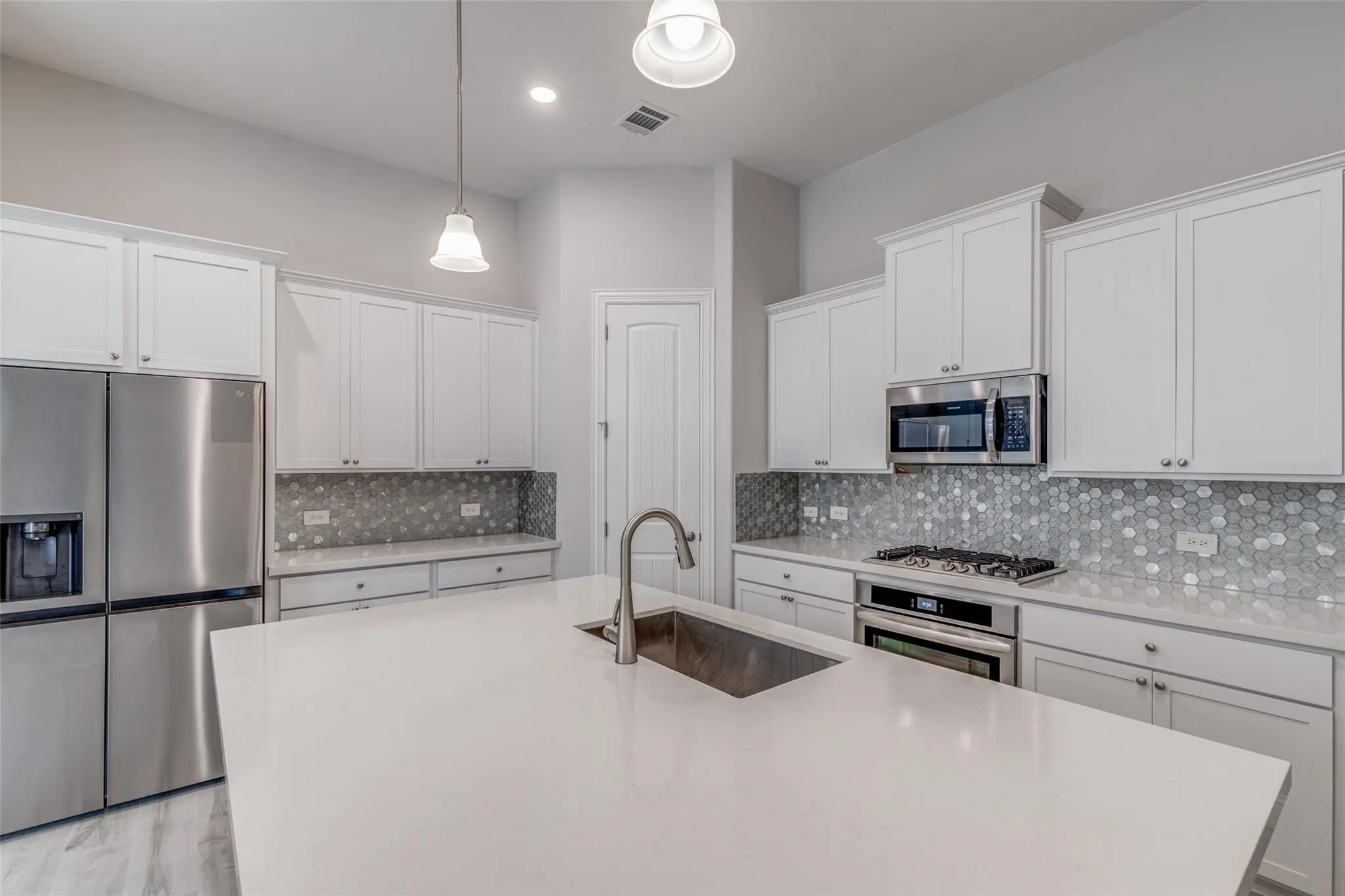 Modern kitchen featuring a large white countertop island with an undermount sink and brushed nickel faucet