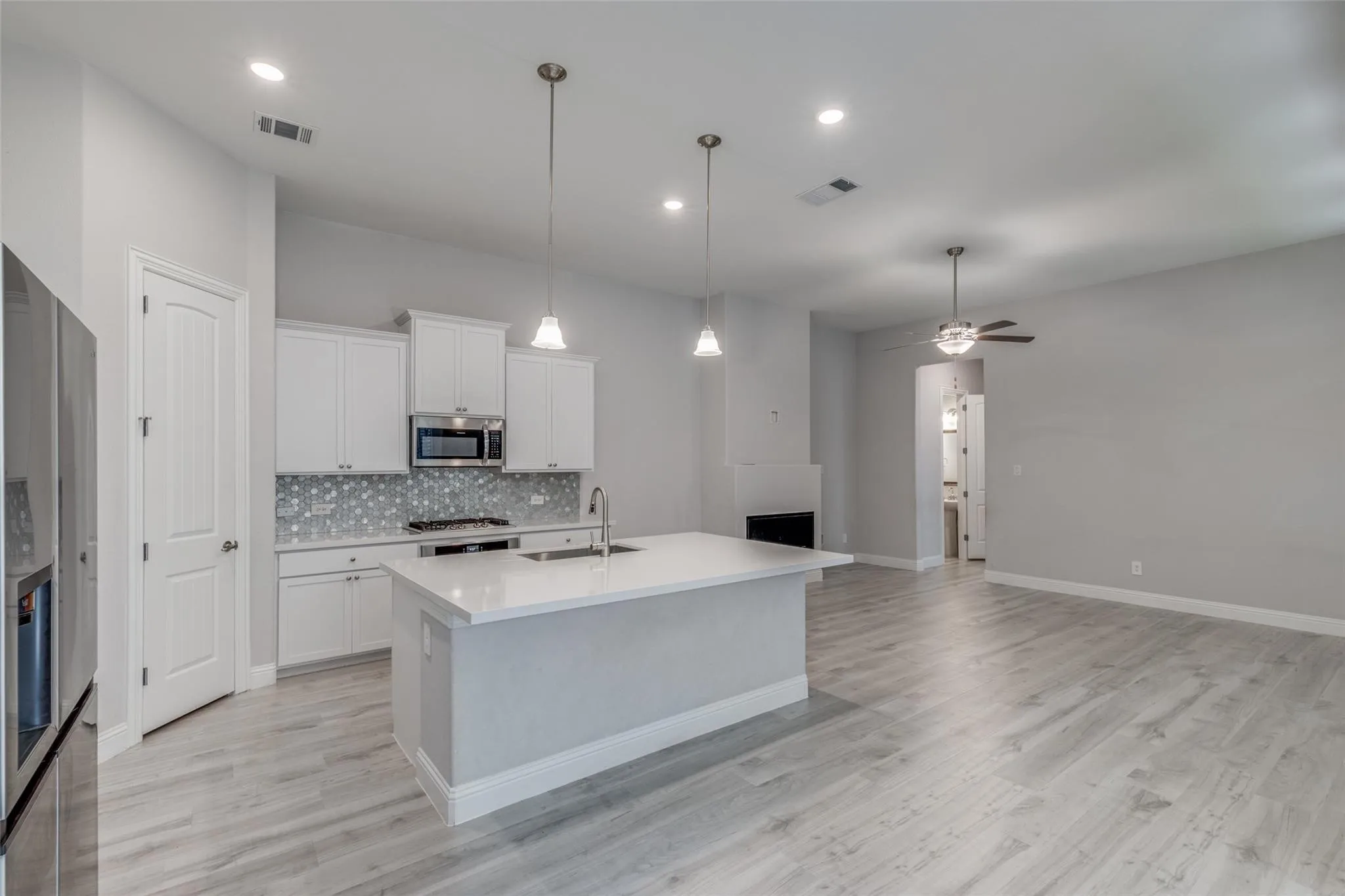 Open-concept kitchen featuring an island with a sink, white cabinetry, a built-in microwave, and a decorative tile backsplash