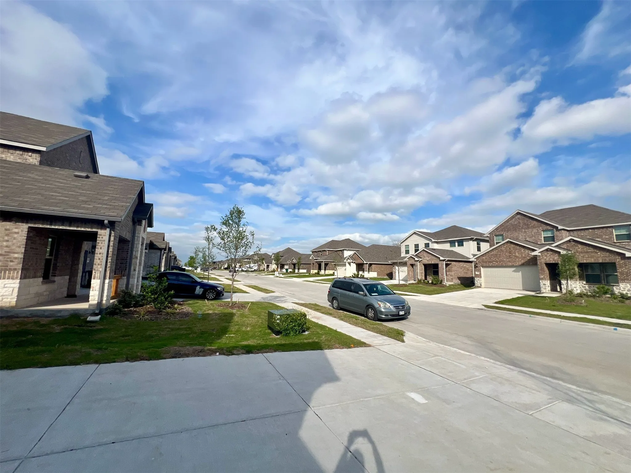 Community streetscape featuring two-story homes with brick and stone exteriors, dark shingle roofs, and attached garages