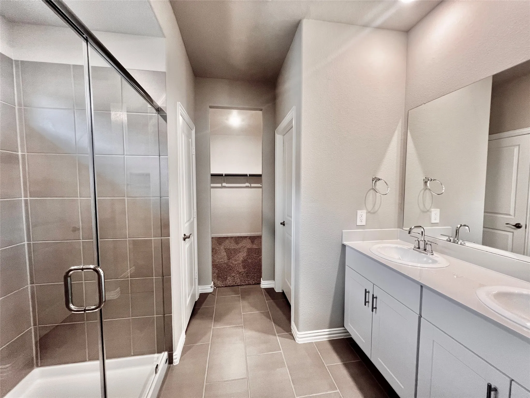 Spacious bathroom featuring a dual vanity, light wood-finish cabinetry, a large frameless mirror, and a glass-enclosed shower with tiled walls