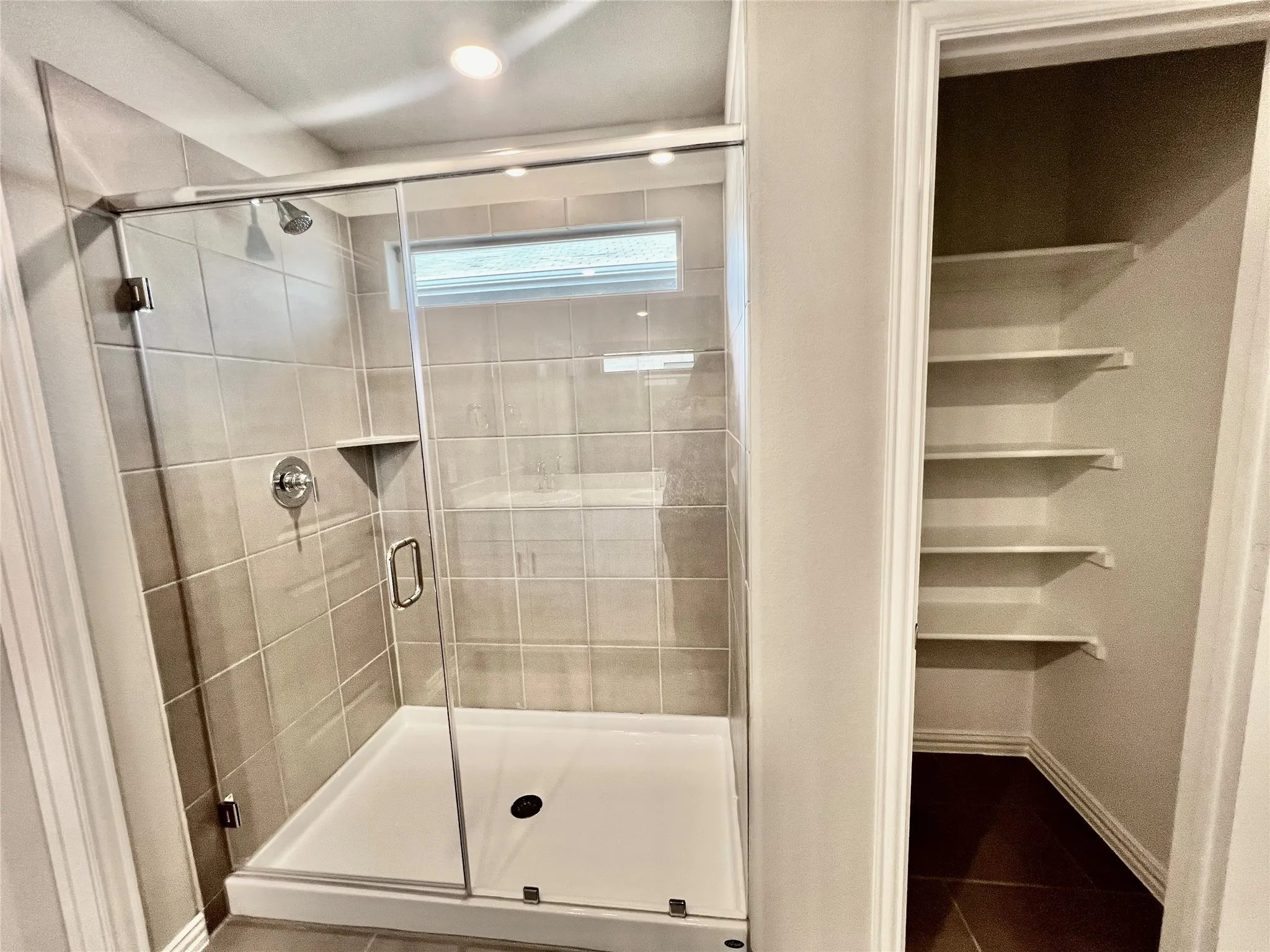 Walk-in shower with clear glass enclosure and light-toned tile surround