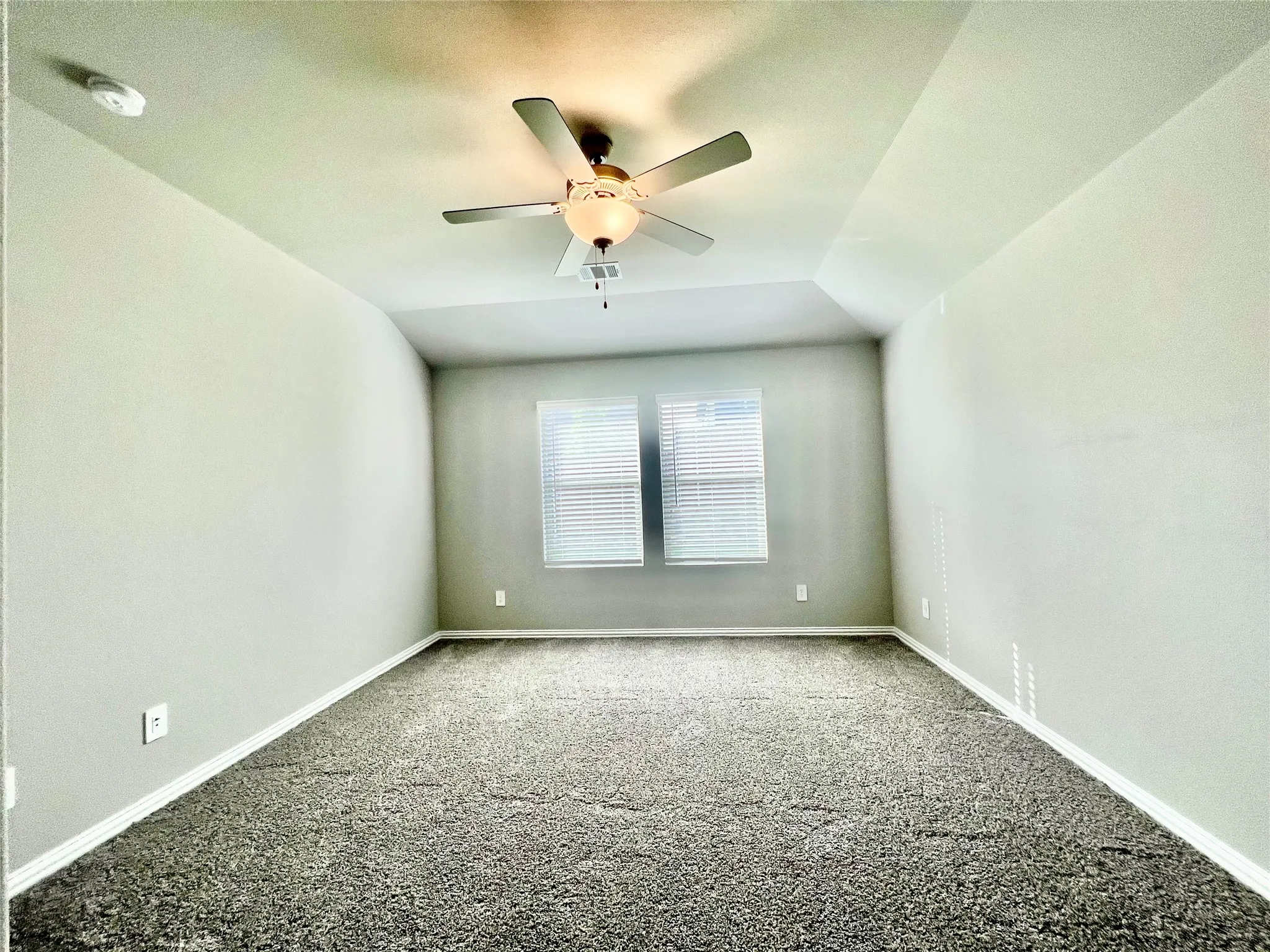 Spacious room featuring vaulted ceilings, light gray wall paint, and dark patterned carpeting