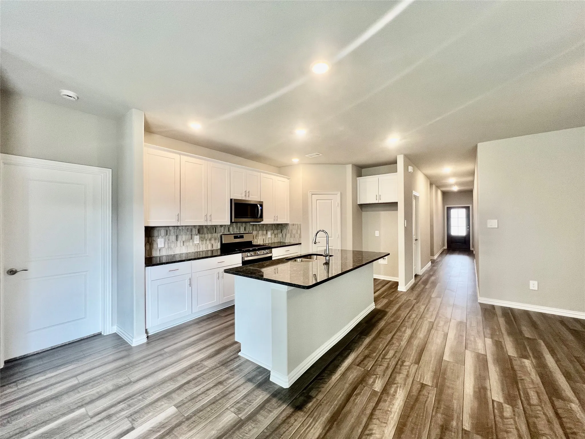 Kitchen featuring a central island with a sink and dark countertop, white cabinetry with silver hardware, an integrated microwave, and a tiled backsplash