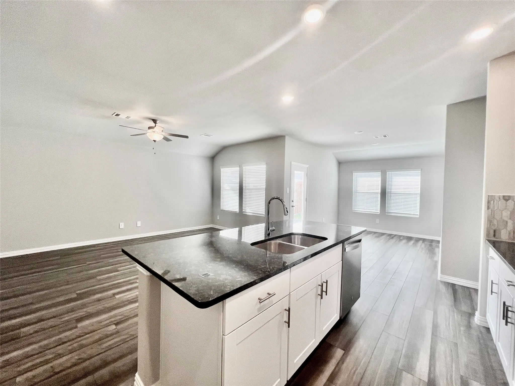 Open-concept kitchen and living area featuring a large center island with a built-in sink and dishwasher, wood-finish flooring, recessed lighting, and multiple windows with blinds