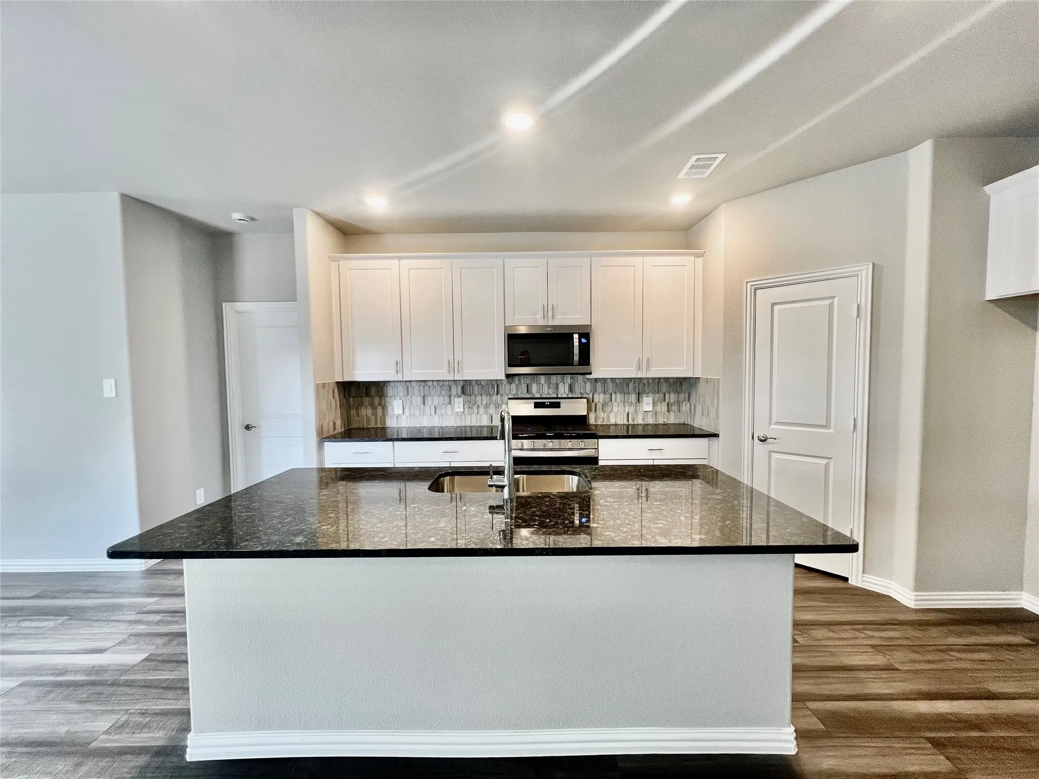Kitchen featuring a large island with a dark countertop, white cabinetry, stainless steel appliances, and a tiled backsplash
