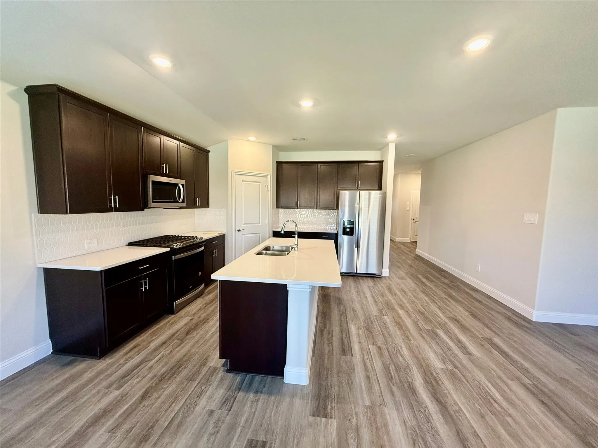 Spacious kitchen featuring dark wood cabinetry, white countertops, stainless steel appliances, a white tile backsplash, and wood-finish flooring
