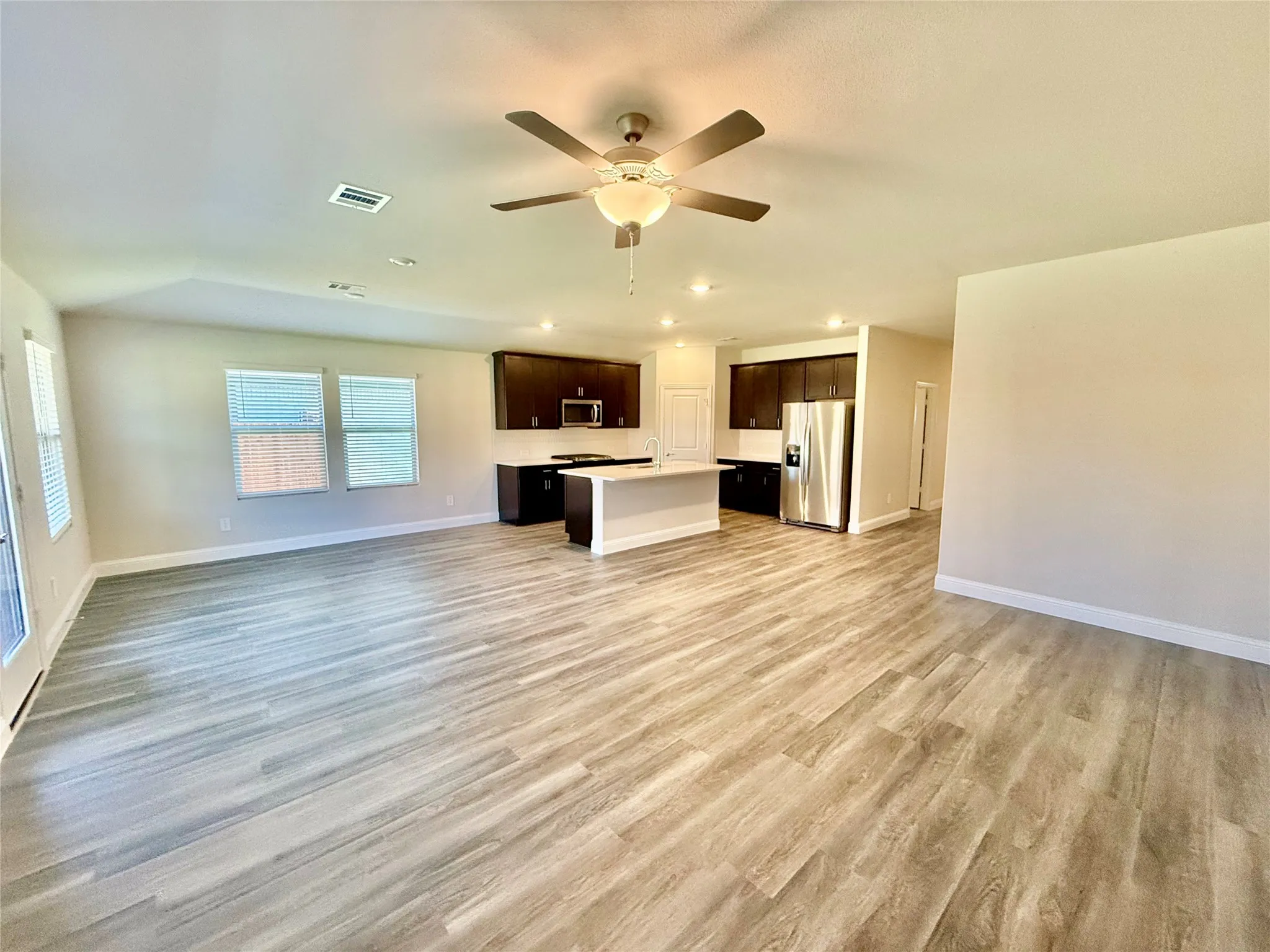 Expansive open-concept living area featuring wood-finish flooring, a kitchen island, recessed lighting, and a ceiling fan