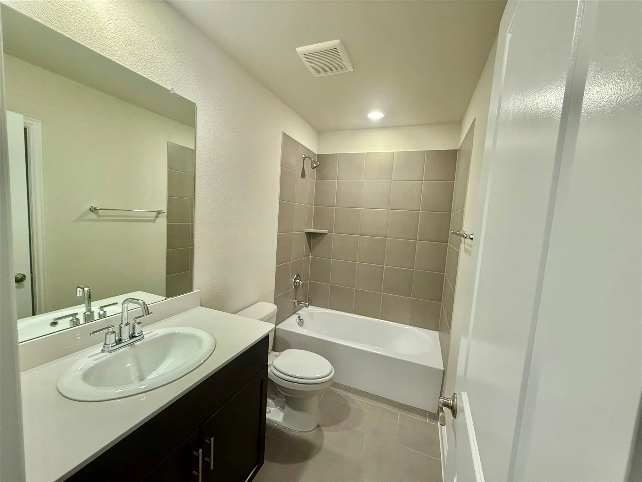 Full bathroom featuring a single vanity with a white countertop and dark wood-finish cabinetry, a toilet, and a bathtub with a tiled shower surround and an integrated shelf
