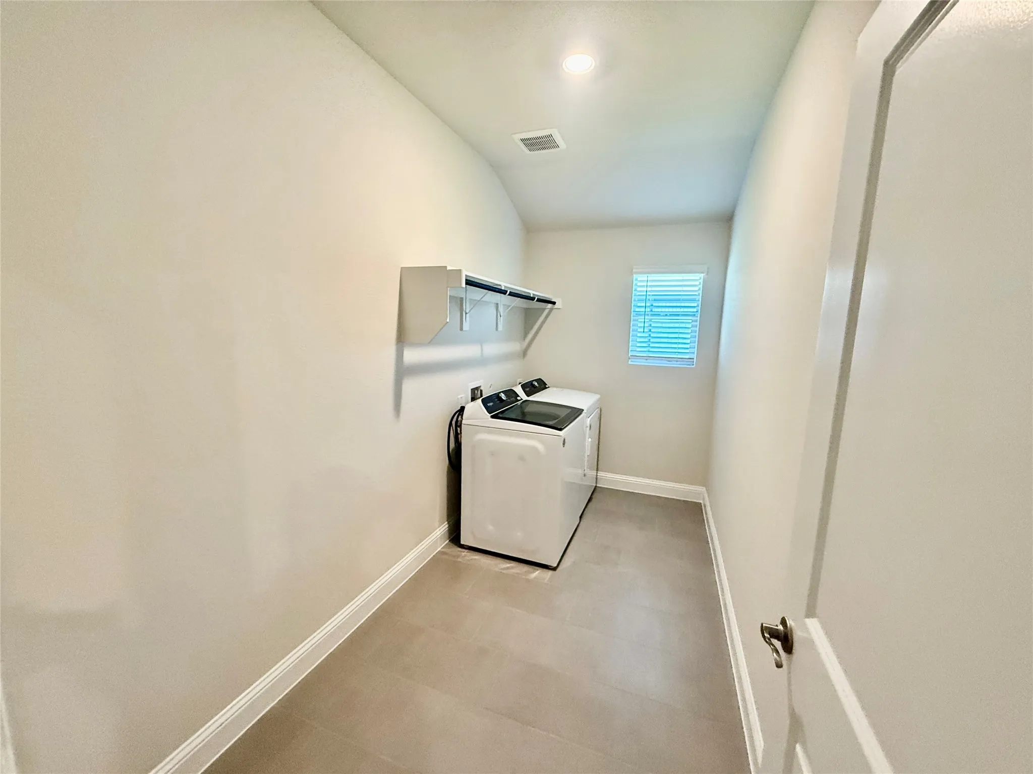 Dedicated utility room featuring tile flooring, a single window with blinds, and built-in shelving