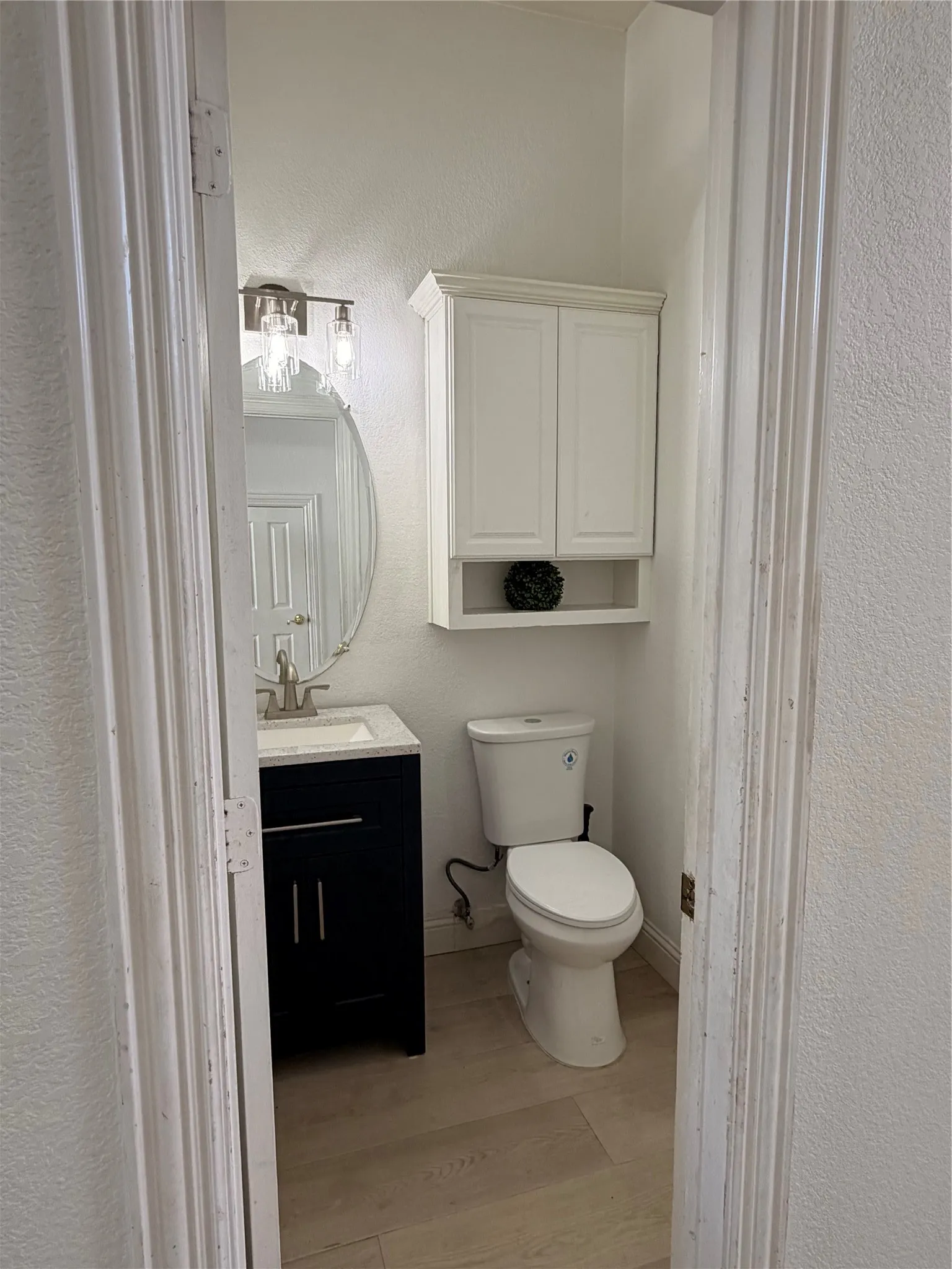 Powder room featuring a dark wood-finish vanity with a light-toned countertop, a contemporary oval mirror, and a sleek two-light vanity fixture