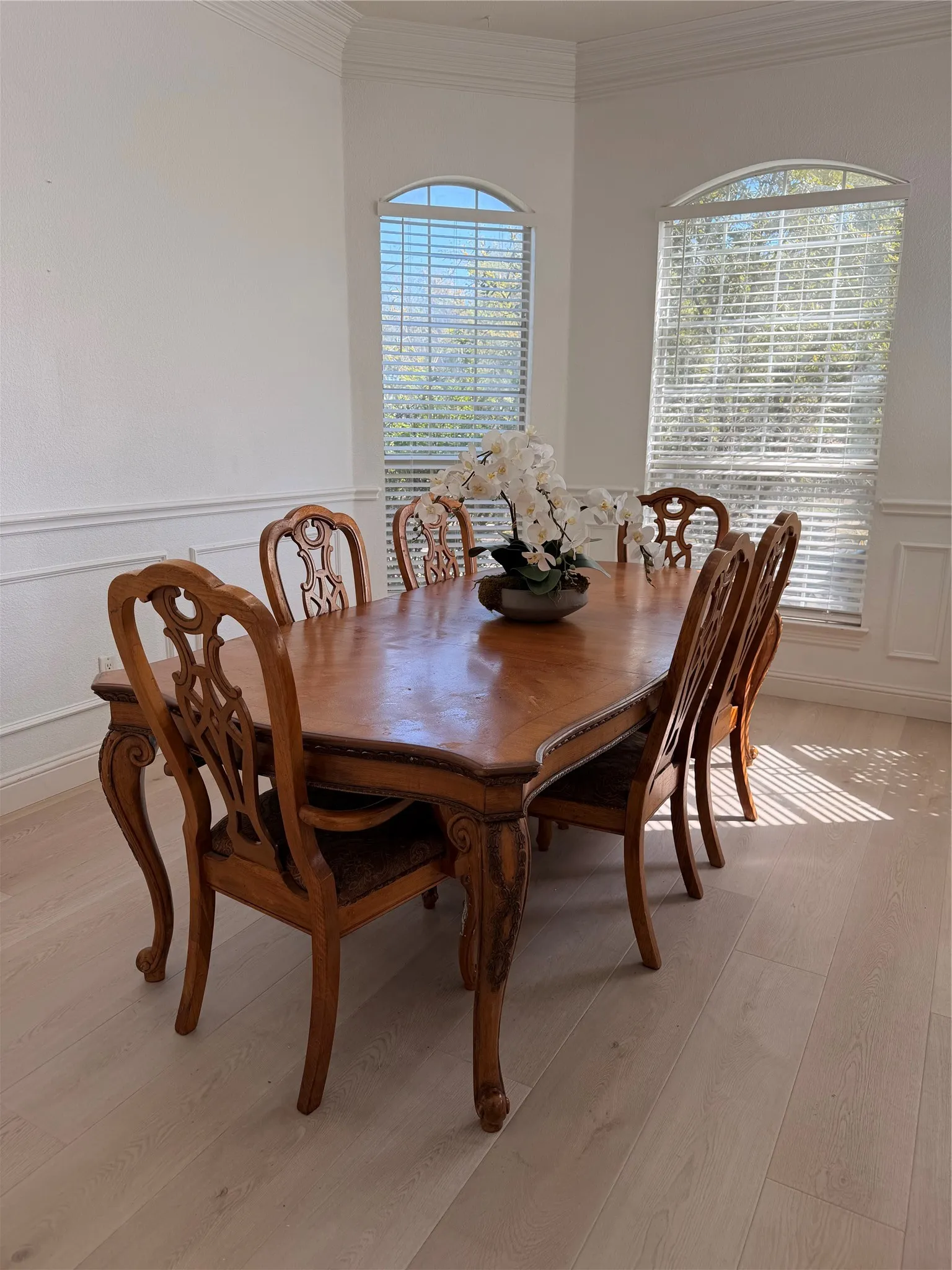 Bright dining area featuring light wood-finish flooring, white wall paneling, and two arched windows with blinds