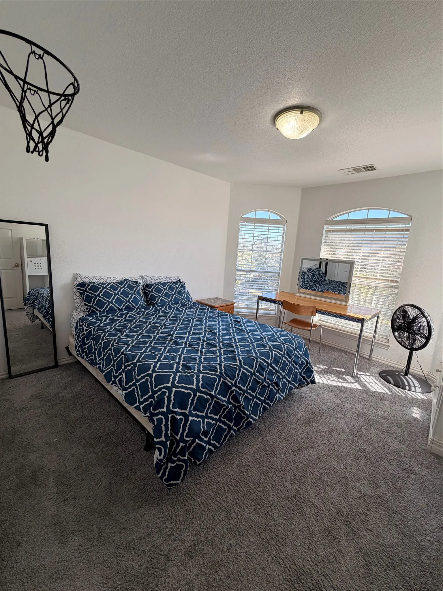 Carpeted bedroom #2 featuring multiple arched windows with blinds, a ceiling-mounted light fixture, and white walls