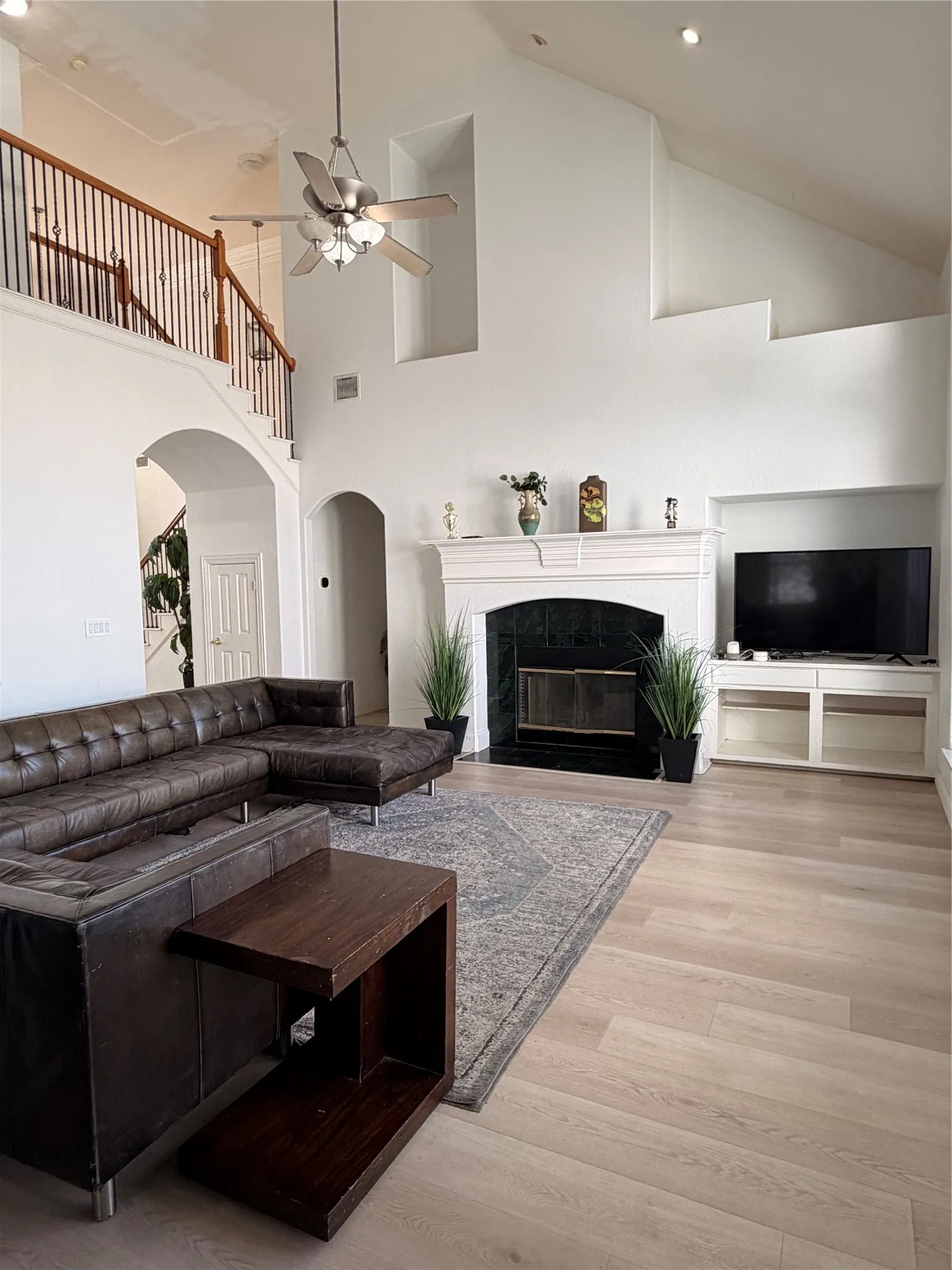 Spacious living area featuring a two-story ceiling, light wood-finish flooring, and a fireplace with a white mantel and dark stone surround