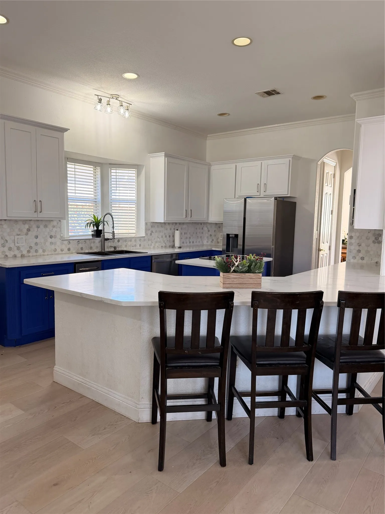 Kitchen featuring light wood-finish flooring, white perimeter cabinetry, blue island cabinetry, and a light-toned countertop