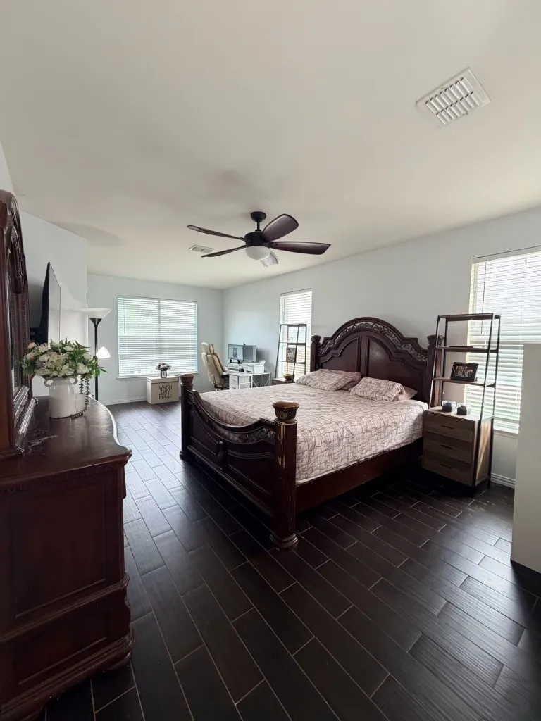 Spacious room featuring dark wood-finish flooring, a ceiling fan, and multiple windows with horizontal blinds