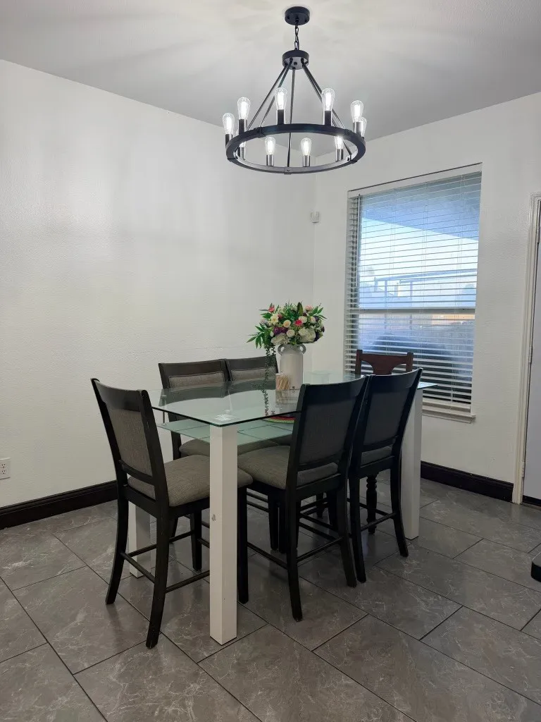 Dining area featuring a contemporary black wagon wheel chandelier, large format tile flooring, and a window with blinds