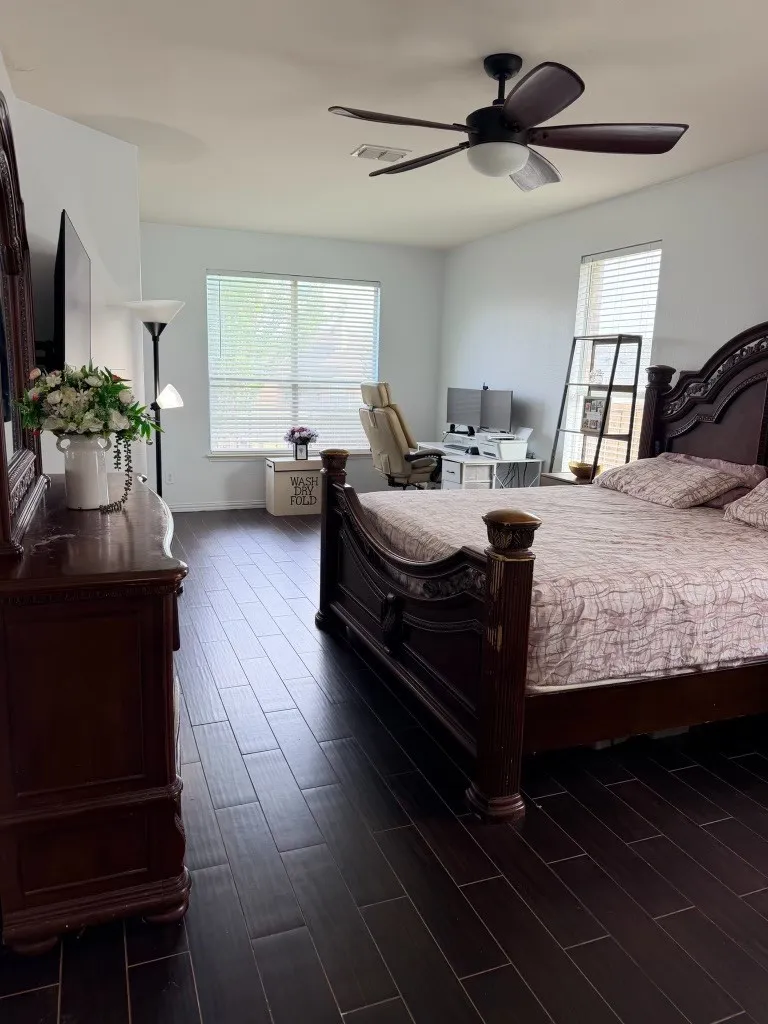 Spacious interior featuring dark wood-finish flooring, a ceiling fan with integrated lighting, and multiple windows with horizontal blinds